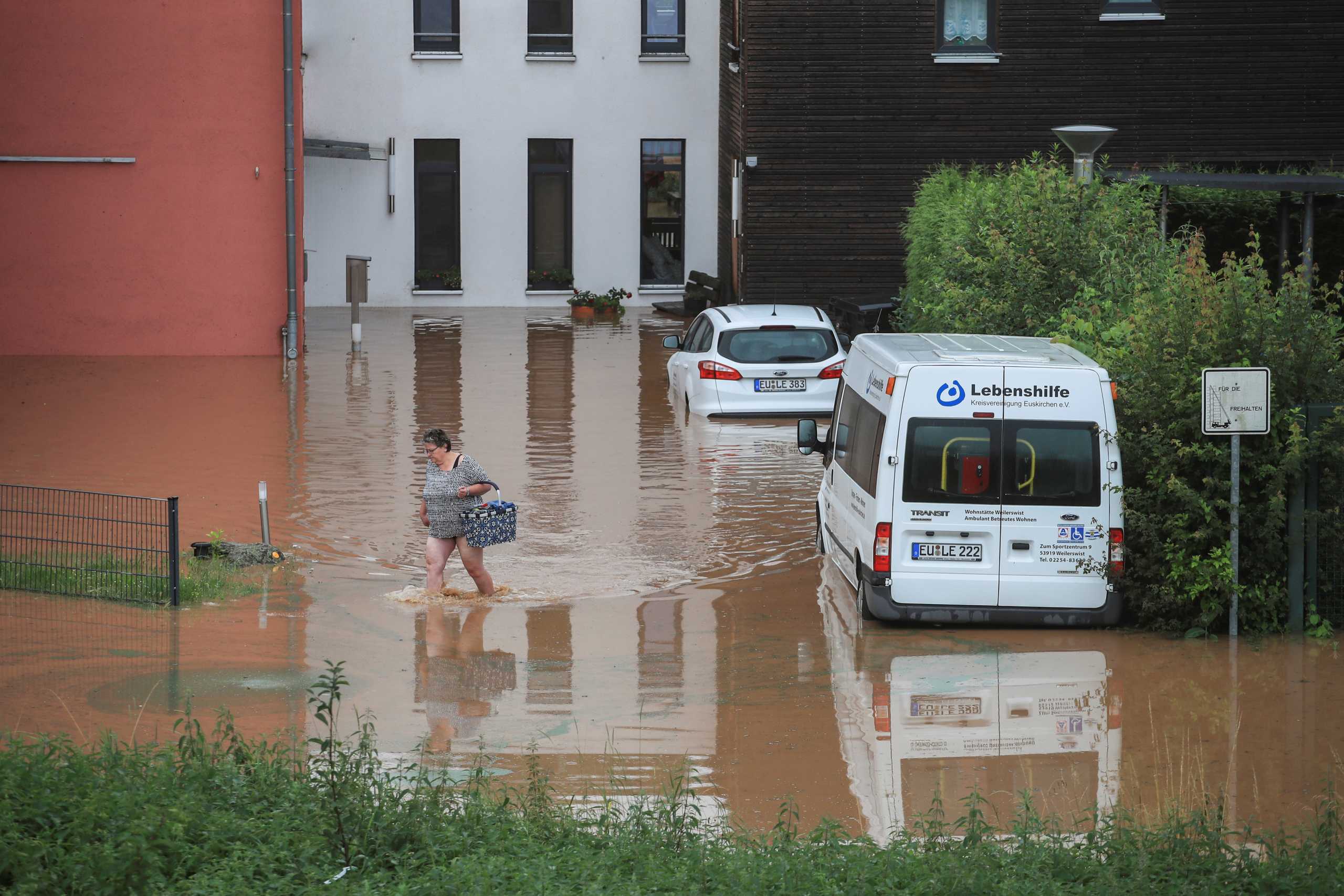 A woman wades across floodwater as she goes out shopping following heavy rainfalls in Gross-Vernich, Germany, July 15, 2021. REUTERS