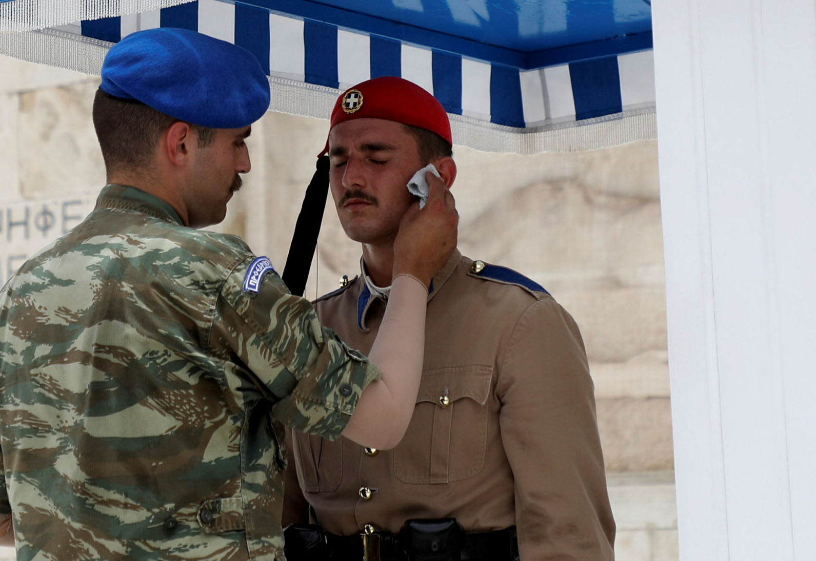 A soldier wipes sweat of a Greek Presidential Guard member in front of the Tomb of the Unknown Soldier during a heatwave, in Athens, Greece, July 1, 2021. REUTERS