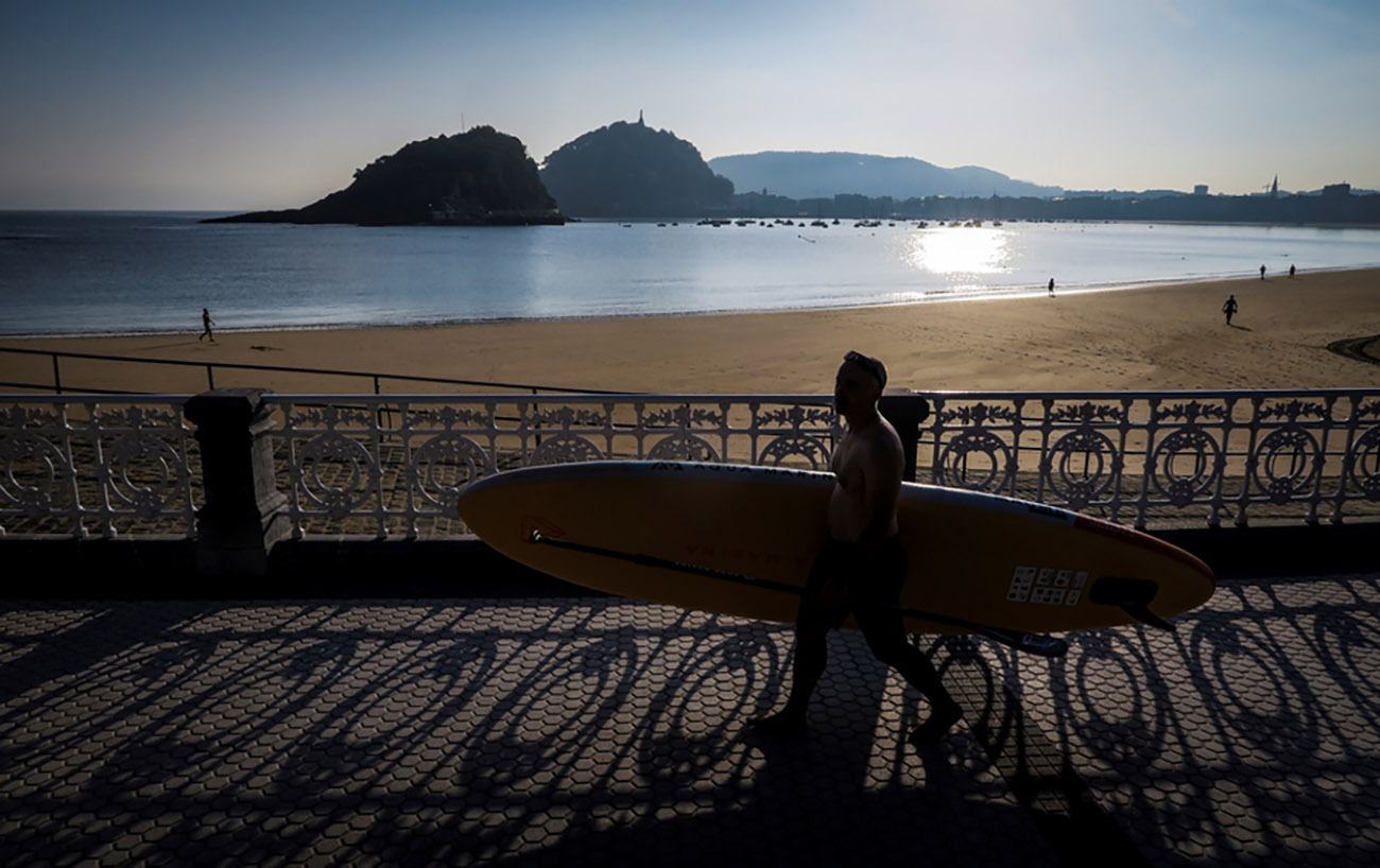 epa09352843 A man on his way to practice paddle surfing, on the beach of Ondarreta in San Sebastian, Spain, 19 July 2021, on a warm morning.  EPA