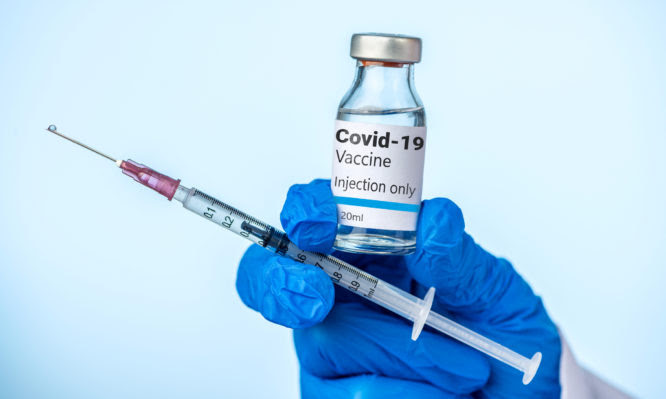 Doctor or nurse is holding the Covid-19 vaccine and syringe with her blue glove.