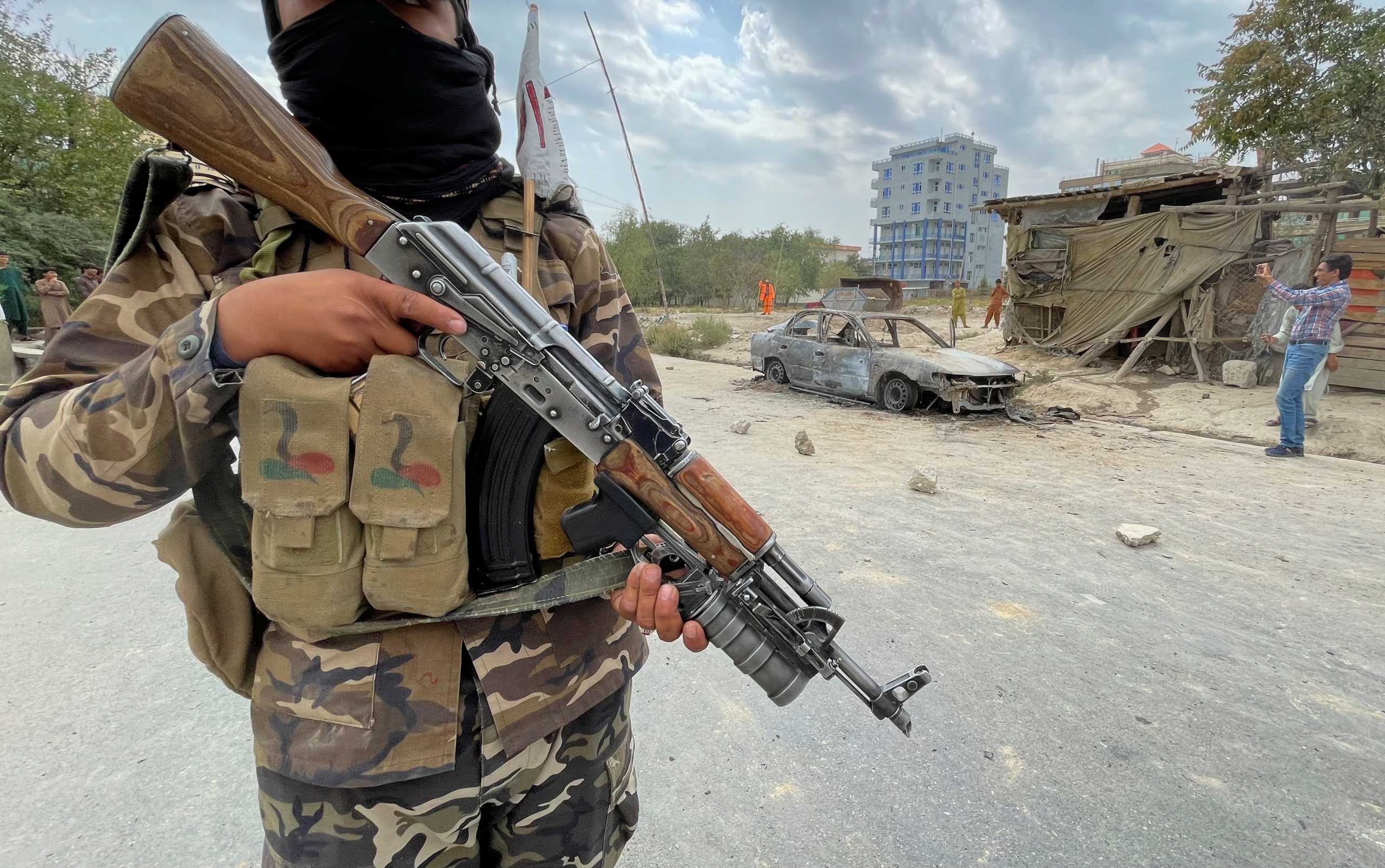 A member of Taliban forces stands guard as Afghan men take pictures of a vehicle from which rockets were fired, in Kabul, Afghanistan August 30, 2021. REUTER