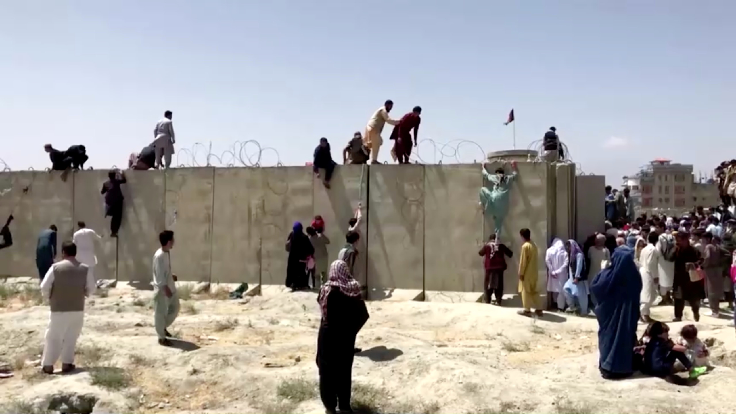 People climb a barbed wire wall to enter the airport in Kabul, Afghanistan August 16, 2021, in this still image taken from a video. REUTERS TV