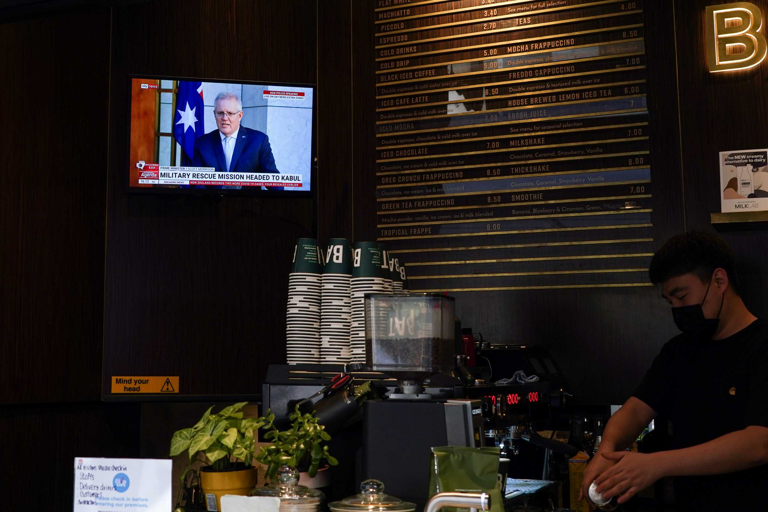 Australian Prime Minister Scott Morrison, speaking about a military rescue mission in Kabul, Afghanistan, is seen on a cafe television as a barista prepares coffees for takeaway service during a lockdown to curb the spread of a coronavirus disease (COVID-19) outbreak in Sydney, Australia, August 18, 2021.  REUTERS