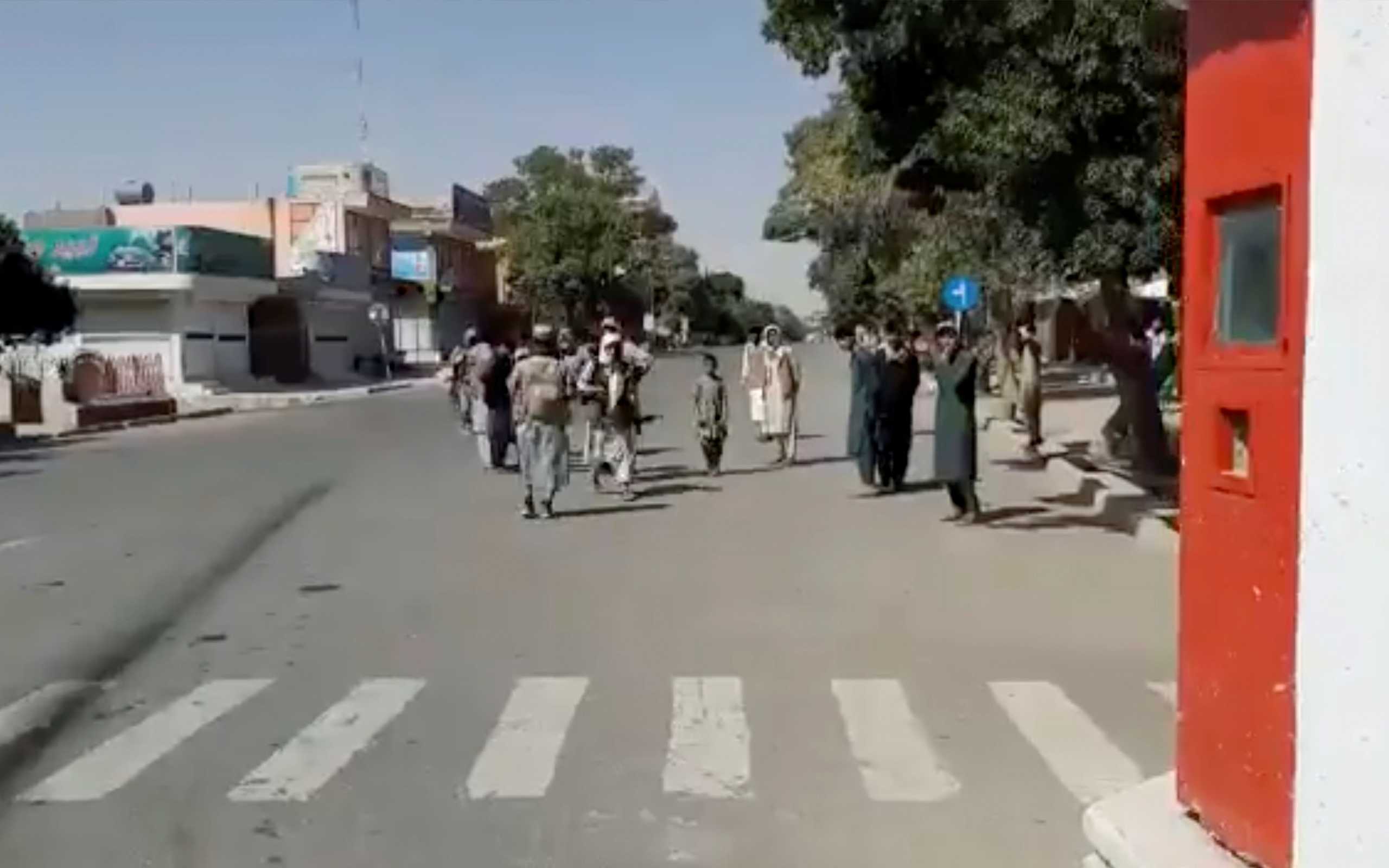 People gather on the street as Taliban fighters stand guard on main road intersection in city of Ghazni, Afghanistan in this screen grab taken from a video released by the Taliban on August 12, 2021. Taliban Handout