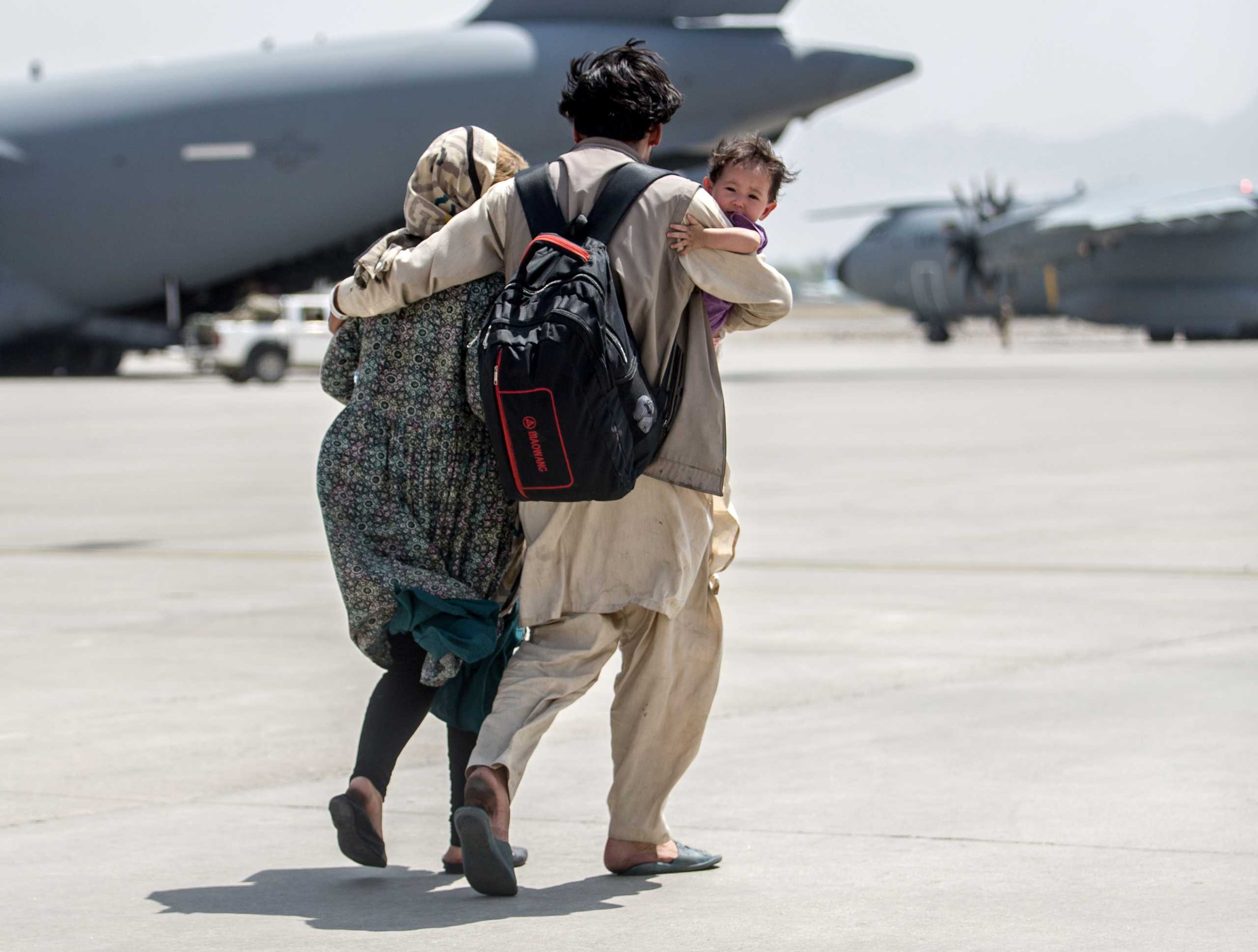 A family walks towards a U.S. Air Force Boeing C-17 Globemaster III during an evacuation at Hamid Karzai International Airport, Afghanistan, August 22, 2021. Picture taken August 22, 2021.  U.S. Marine Corps