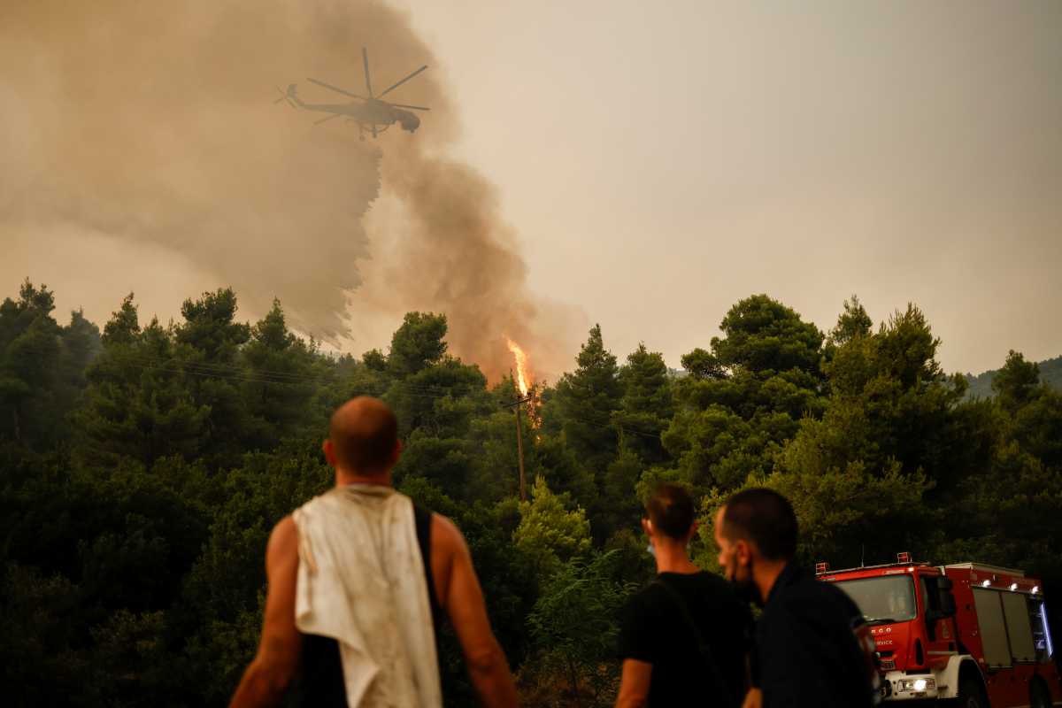 A firefighting helicopter makes a water drop as a wildfire burns in the village of Vilia, Greece, August 18, 2021. REUTERS