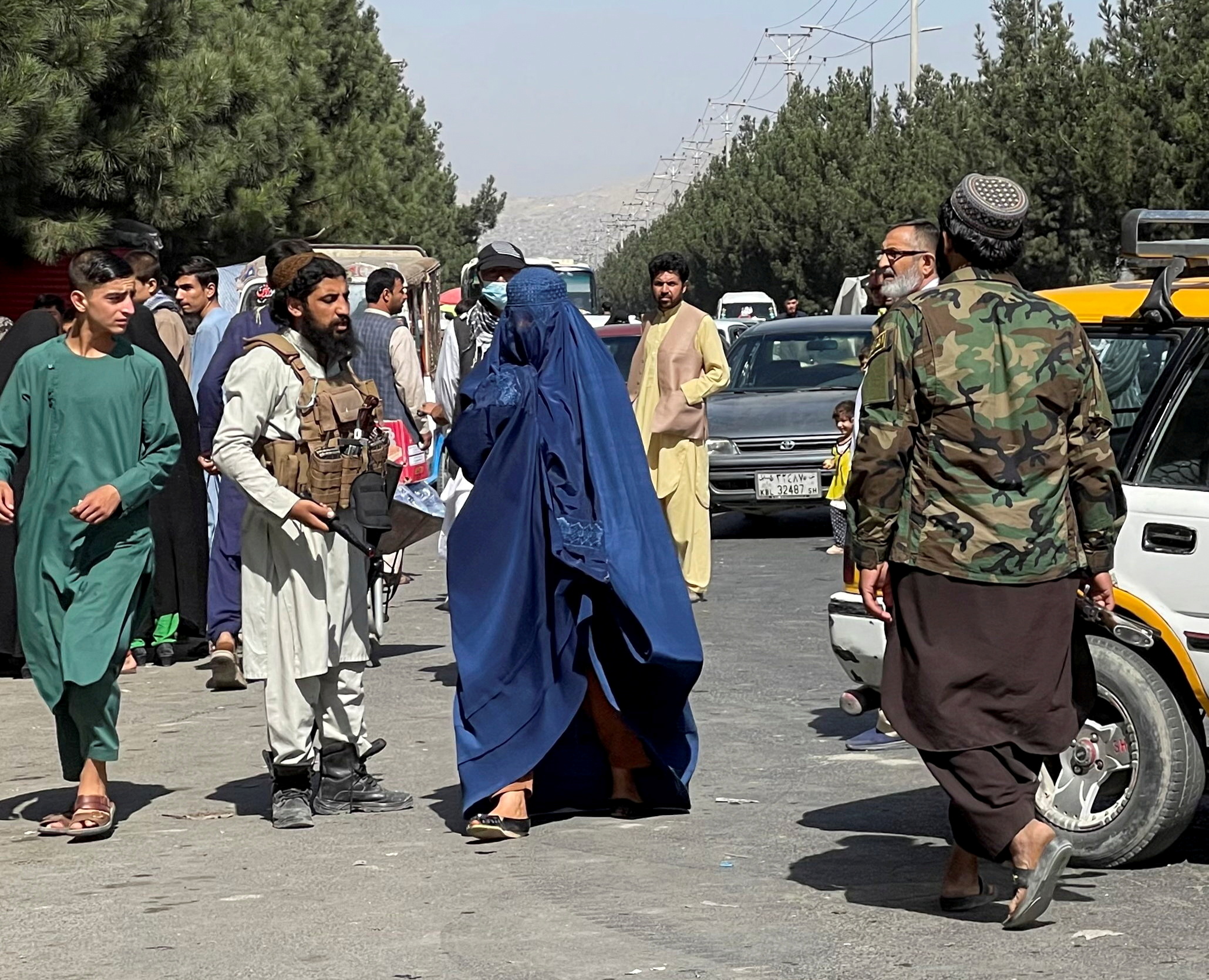 FILE PHOTO: Taliban forces block the roads around the airport, while a woman with Burqa walks passes by, in Kabul, Afghanistan. August 27, 2021. REUTER