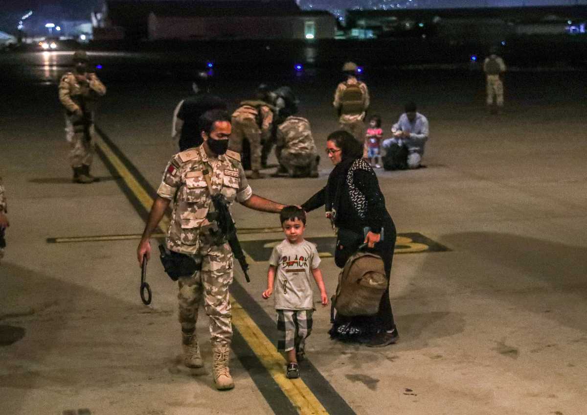FILE PHOTO: A member of the Qatar Air force walks next to a boy evacuated from Afghanistan, at Al-Udeid airbase in Doha, Qatar in this recent undated handout. Government Communications Office of the State of Qatar