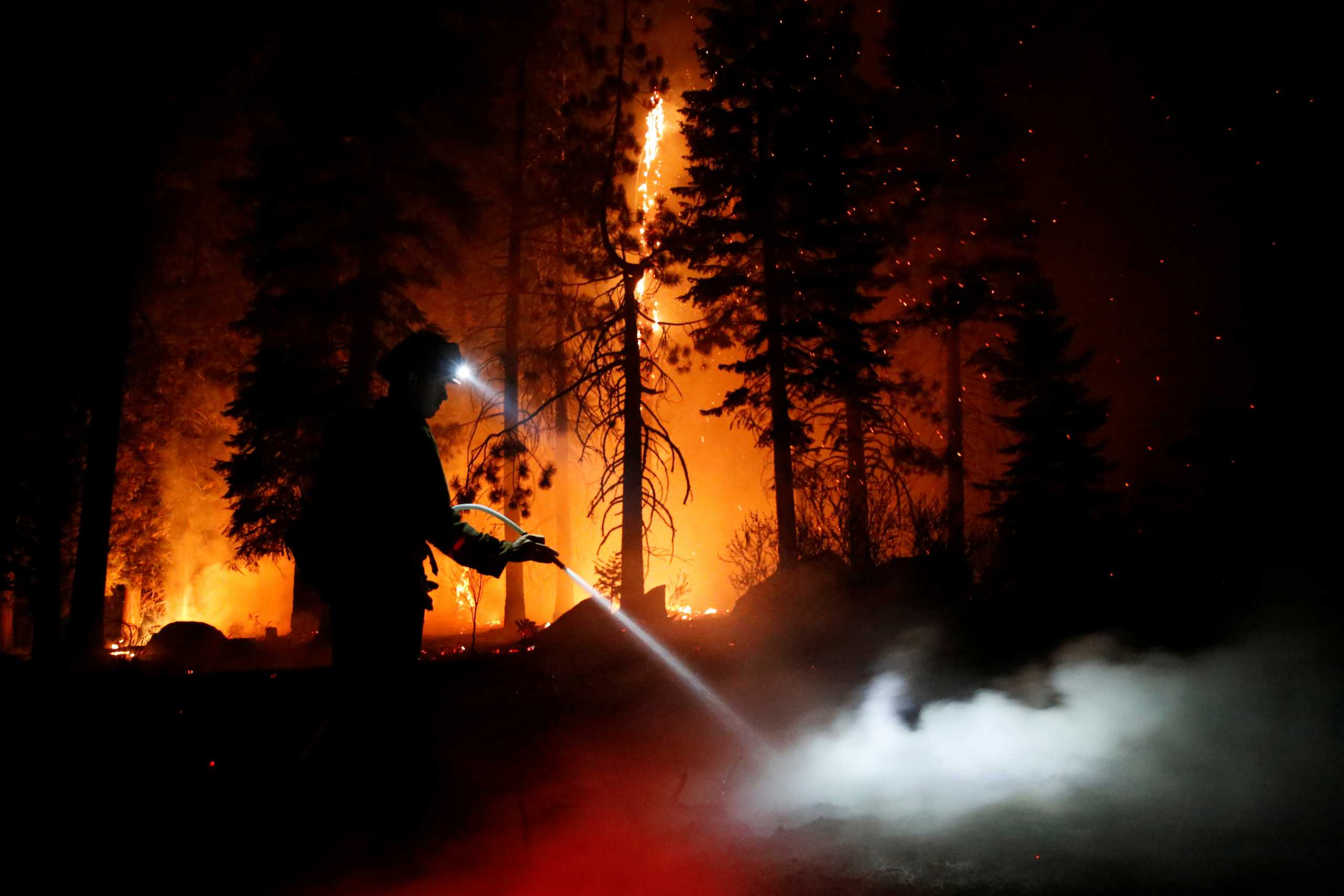 Patrick R., 27, a firefighter with Cal Fire sprays water on hot spots as flames from the Caldor Fire burn through trees in Christmas Valley near South Lake Tahoe, California, U.S., August 31, 2021.    REUTERS