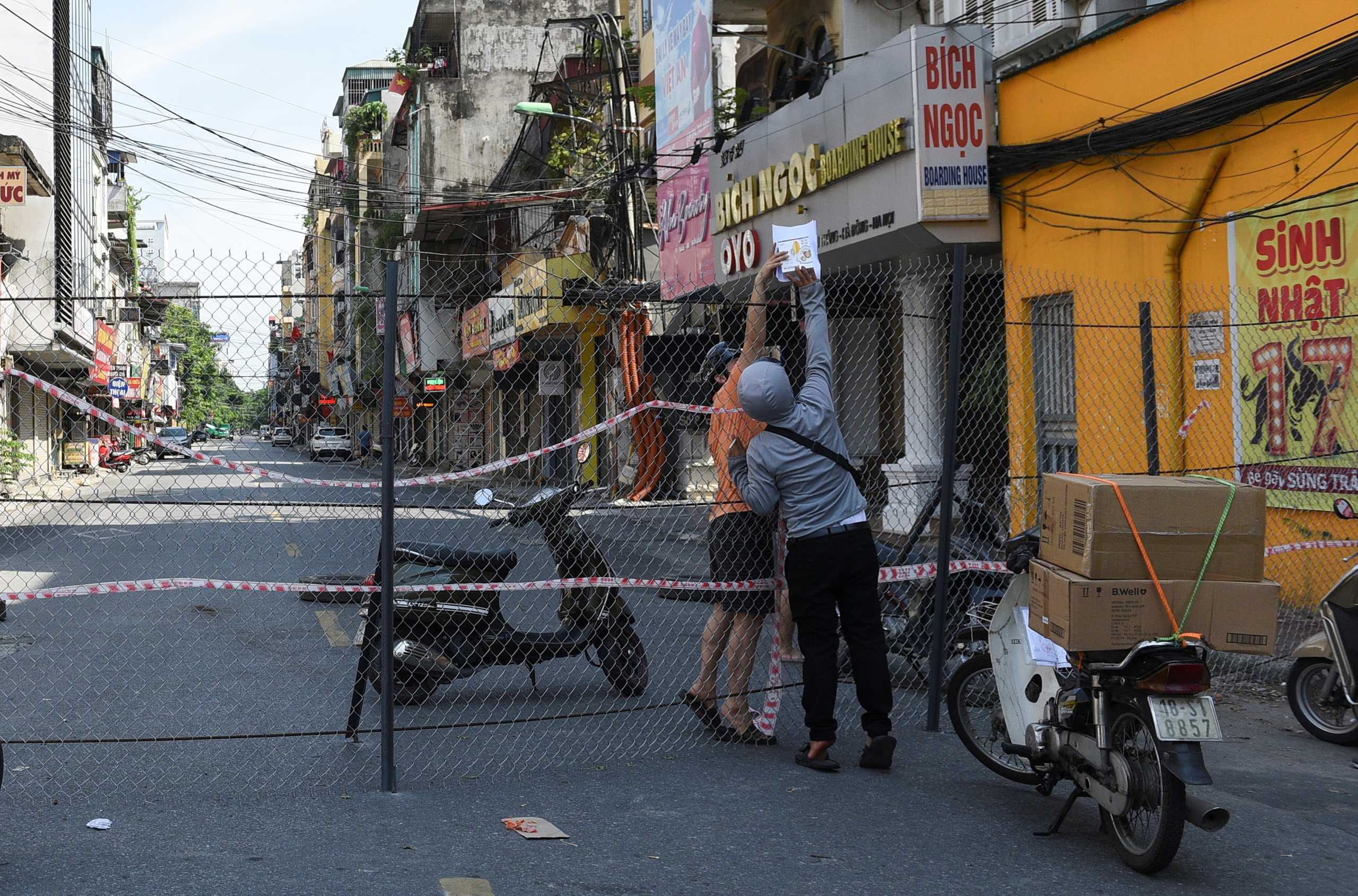 A man picks up groceries through a barrier in a quarantine area amid the coronavirus disease (COVID-19) in Hanoi, Vietnam, September 6, 2021.REUTERS