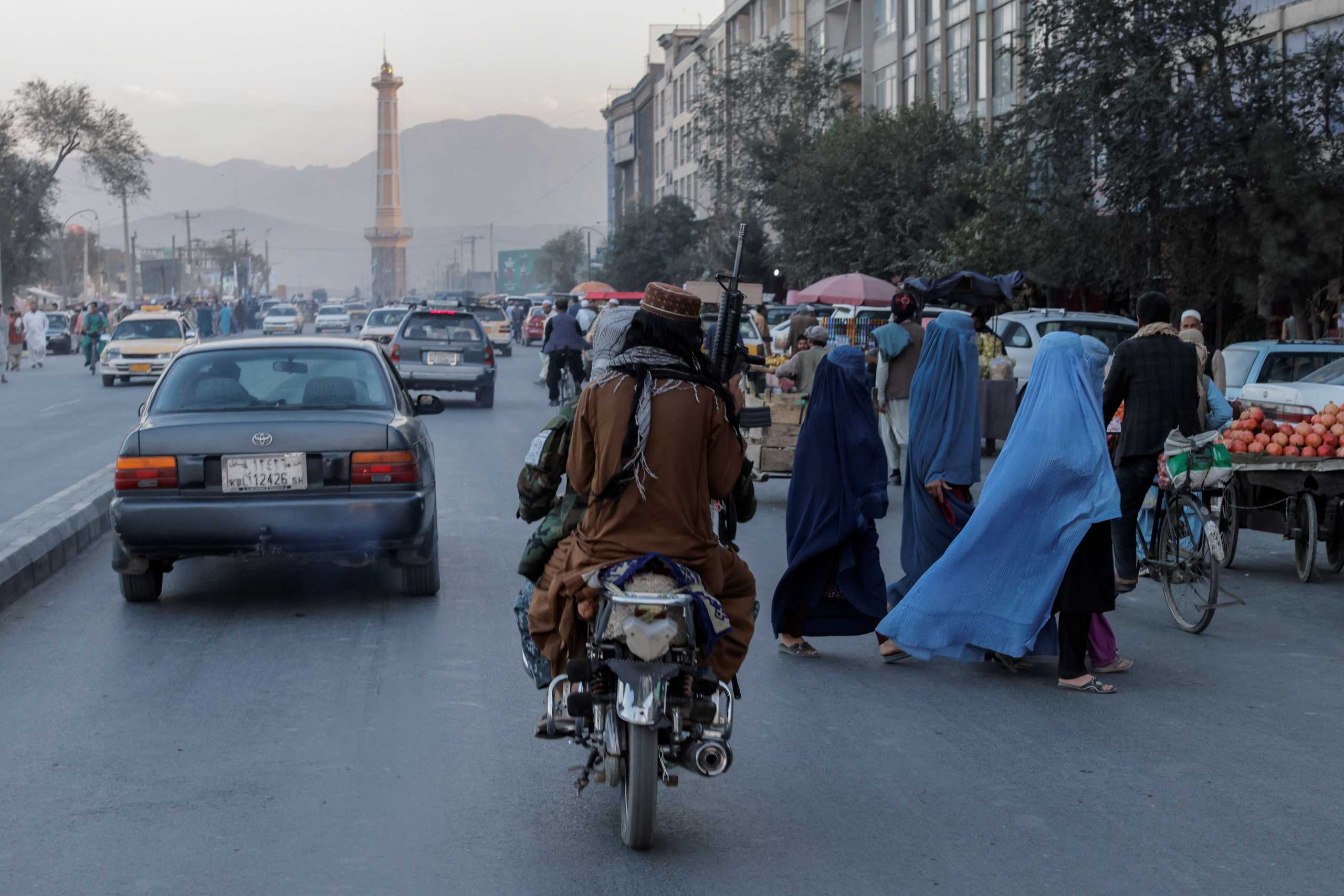 A group of women wearing burqas crosses the street as members of the Taliban drive past in Kabul, Afghanistan October 9, 2021. REUTERS