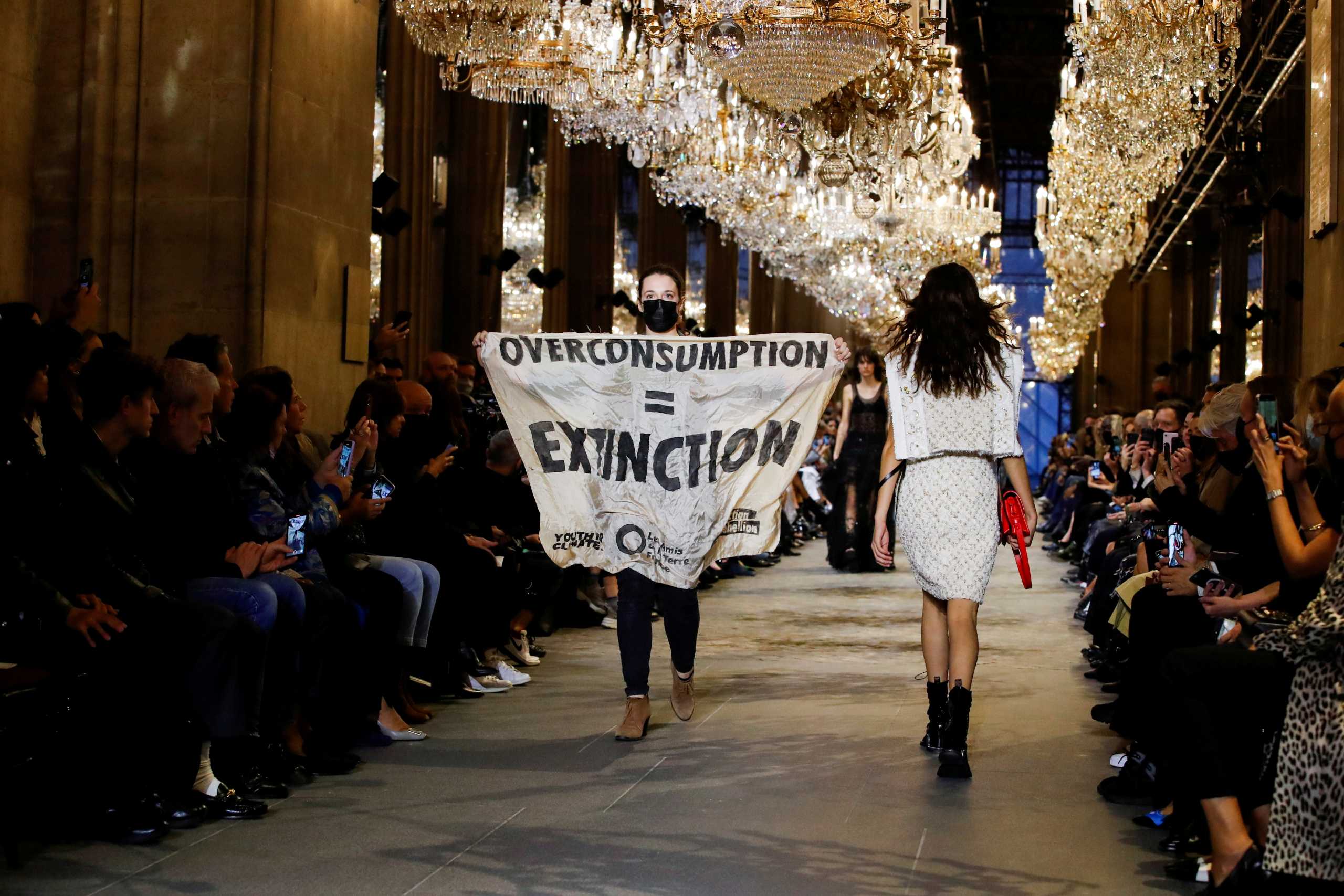 An activist walks on the ramp with a banner that says "Overconsumption = Extinction" as she crashes the designer Nicolas Ghesquiere Spring