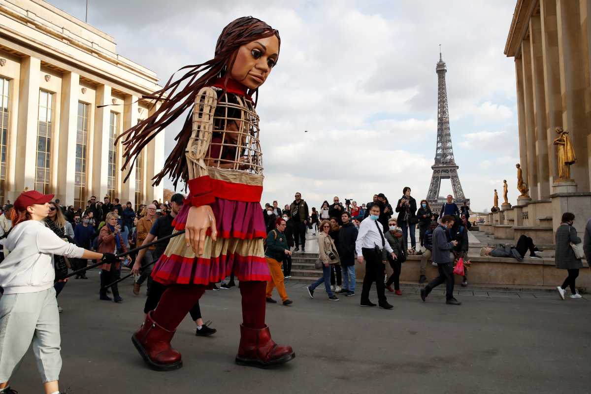 People gather around "Little Amal", a 3.5 metre tall puppet of a young Syrian refugee girl, as part of its 8,000 km tour across Europe from Turkey to Britain to raise awareness for the plight of young refugees, during a walk at Trocadero square near the Eiffel tower in Paris, France, October 15, 2021. REUTERS