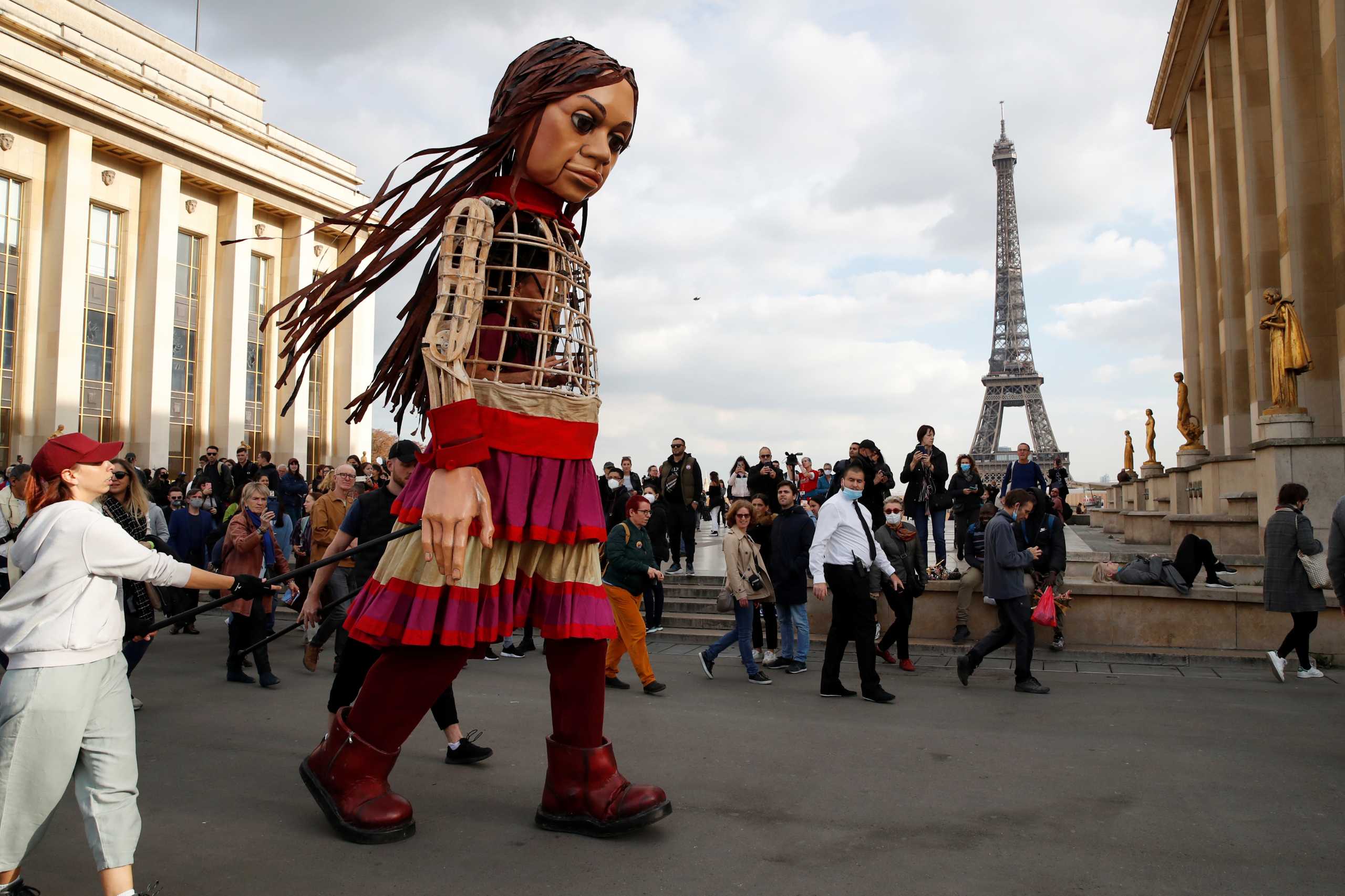 People gather around "Little Amal", a 3.5 metre tall puppet of a young Syrian refugee girl, as part of its 8,000 km tour across Europe from Turkey to Britain to raise awareness for the plight of young refugees, during a walk at Trocadero square near the Eiffel tower in Paris, France, October 15, 2021. REUTERS