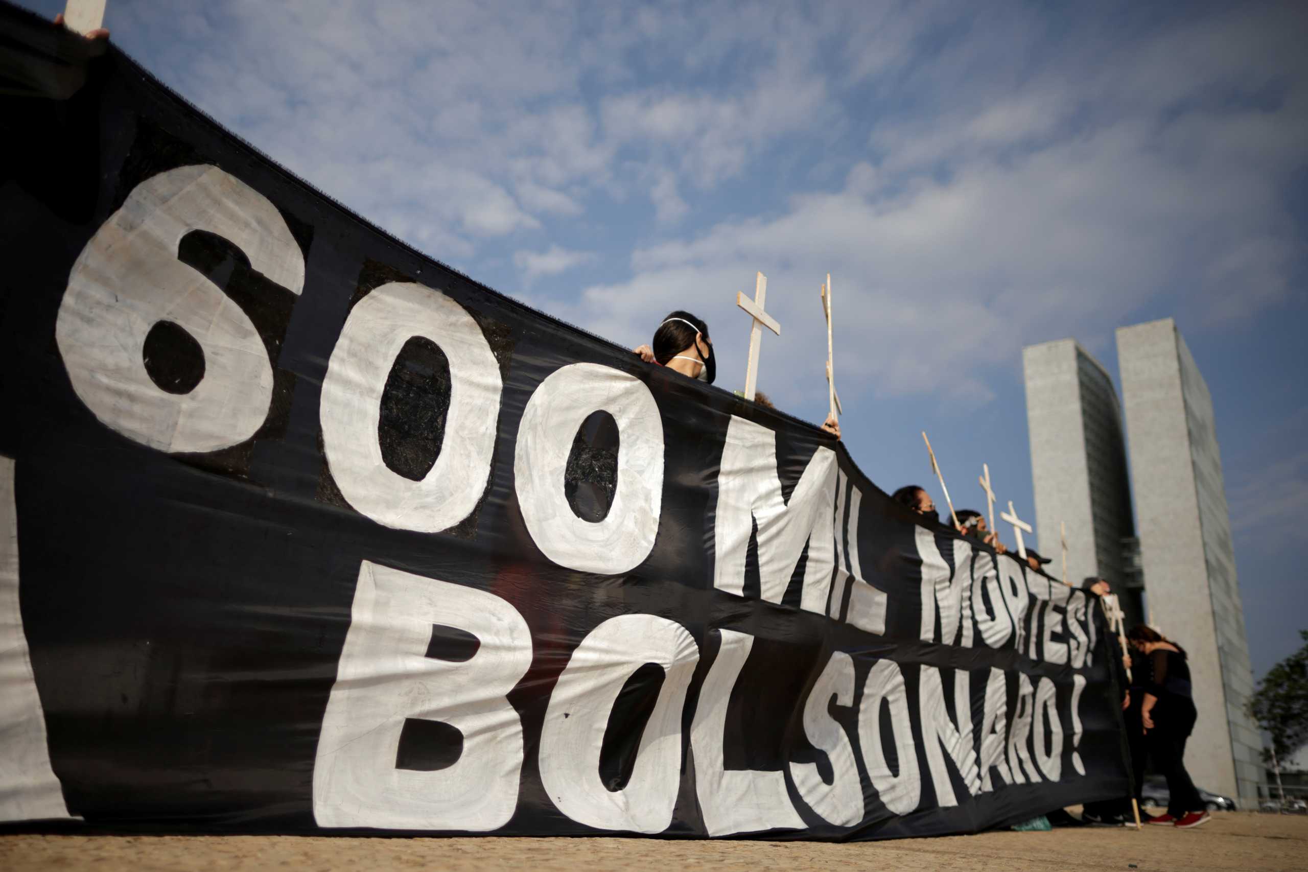 FILE PHOTO: Demonstrators hold a banner and crosses during a protest to pay tribute to Brazil's 600,000 COVID-19 deaths and against Brazil's President Jair Bolsonaro's handling of the coronavirus disease pandemic, in Brasilia, Brazil October 8, 2021. REUTERS