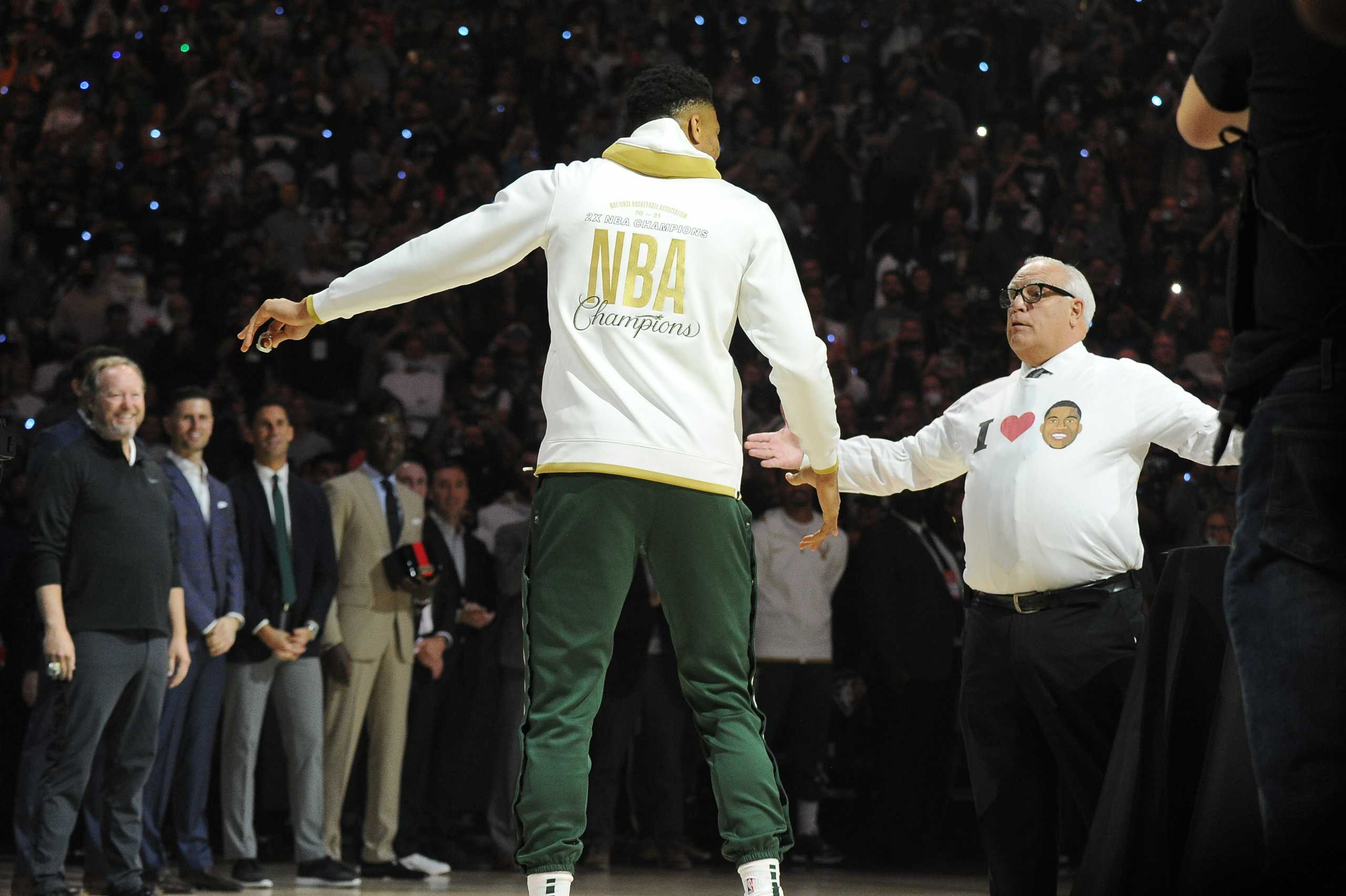 Oct 19, 2021; Milwaukee, Wisconsin, USA;  Former announcer Jim Paschke shows Milwaukee Bucks forward Giannis Antetokounmpo (34) his shirt after receiving his NBA championship ring at Fiserv Forum. Mandatory Credit: Michael McLoone-USA TODAY Sports