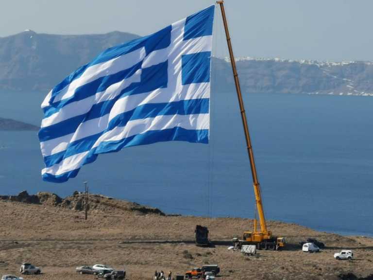 Σαντορίνη: Περήφανη κυματίζει η μεγαλύτερη ελληνική σημαία – Την ύψωσαν με γερανό