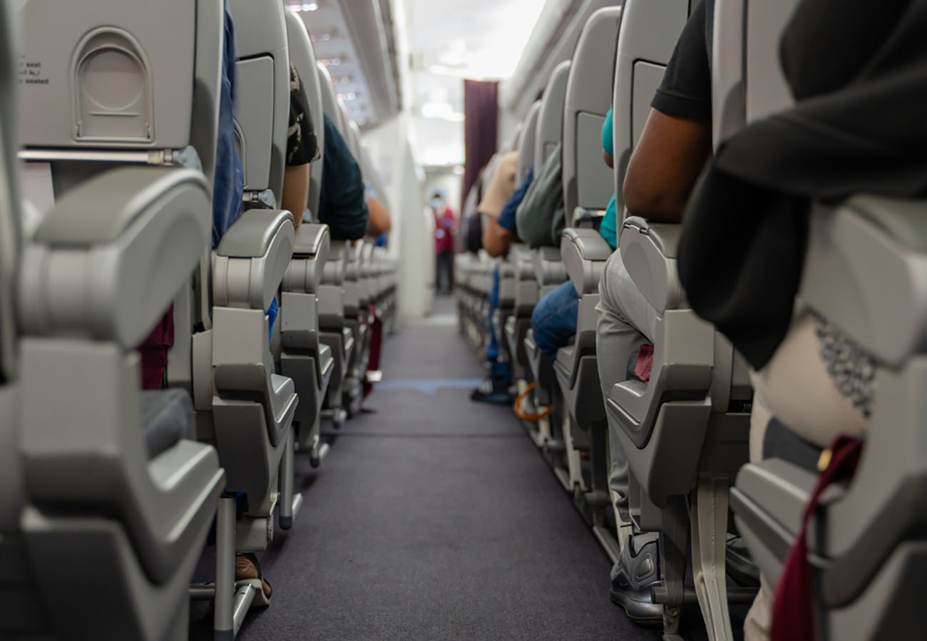 passenger seat, Interior of airplane with passengers sitting on seats and stewardess walking the aisle in background. Selective Focus
