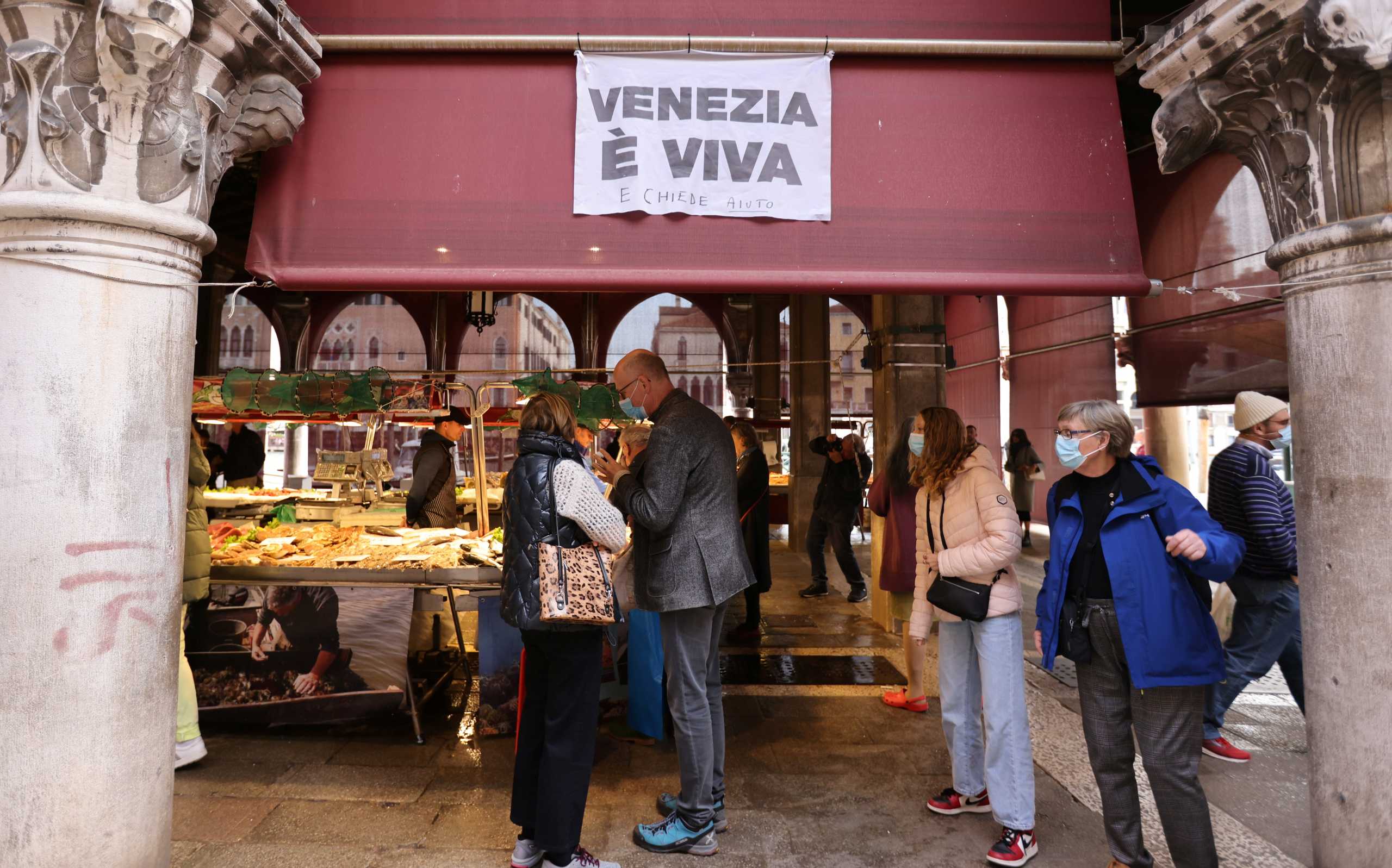 People wear face masks amid the coronavirus disease (COVID-19) outbreak at the fish market near Rialto bridge in Venice, Italy, October 19, 2021. The sign reads 'Venice is alive and asks for help'.  REUTERS