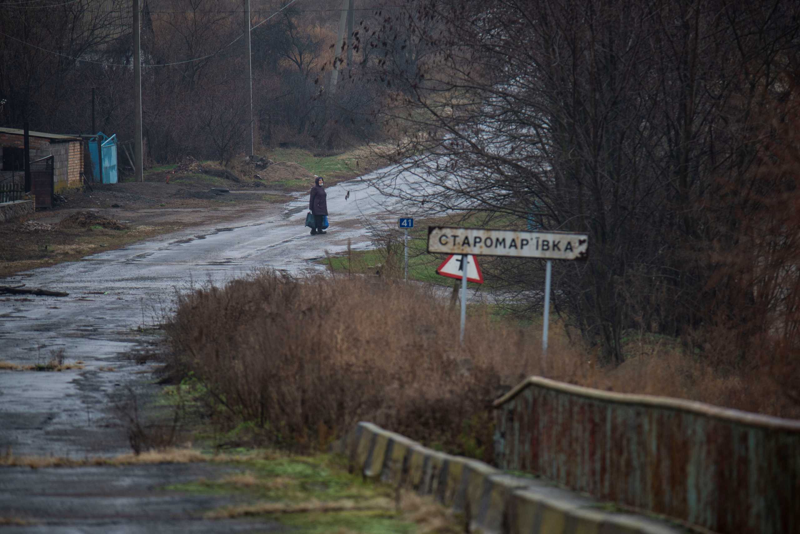 A woman stands on a road in the village of Staromarivka located on the separation line that divides Ukraine between government-controlled territory and the enclave controlled by Russian-backed separatist forces, in Donetsk Region, Ukraine November 23, 2021. Irina Rybakova