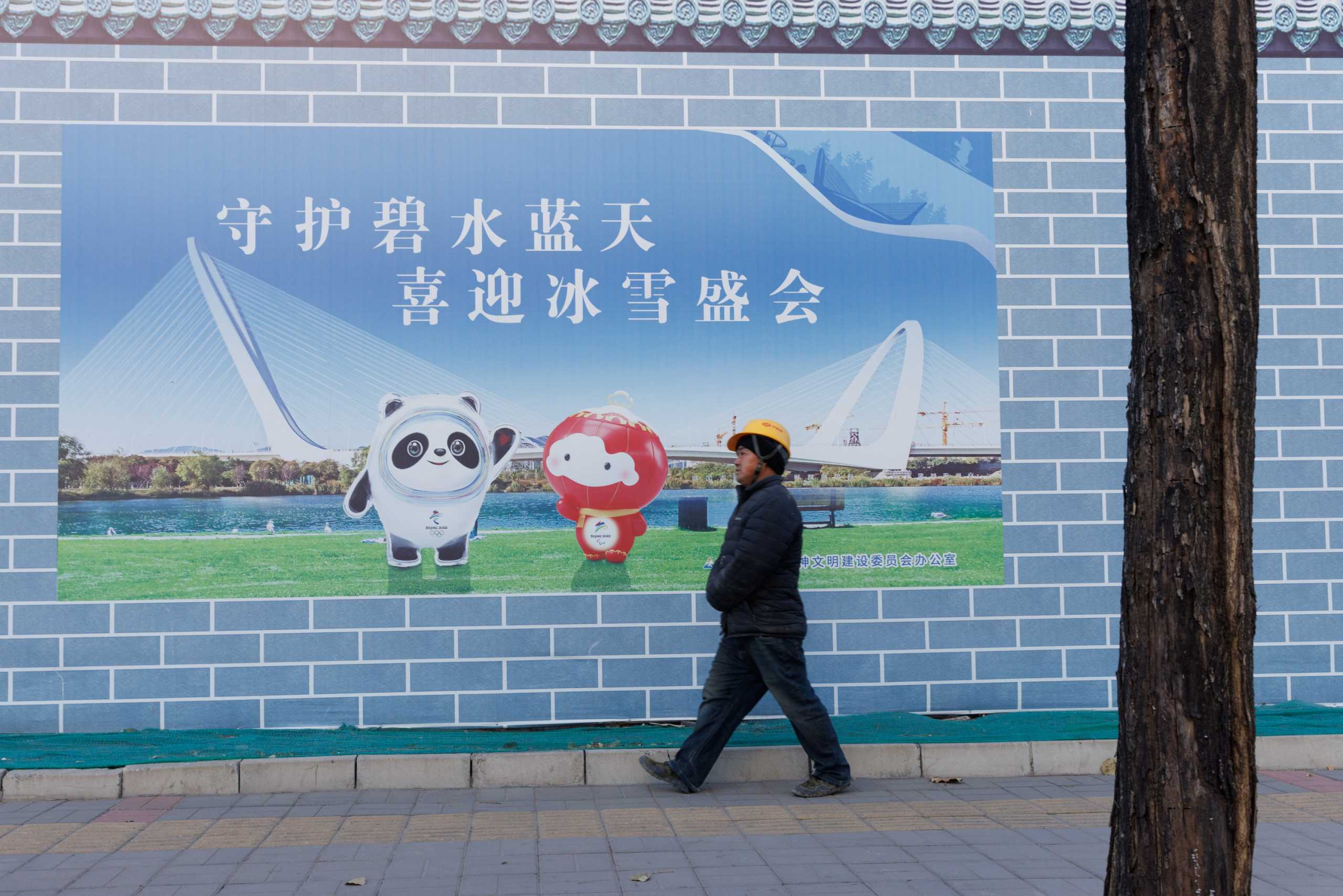 A worker walks past a poster showing the mascots of the Beijing 2022 Olympic and Paralympic Winter Games in Beijing, China, November 30, 2021.  REUTERS