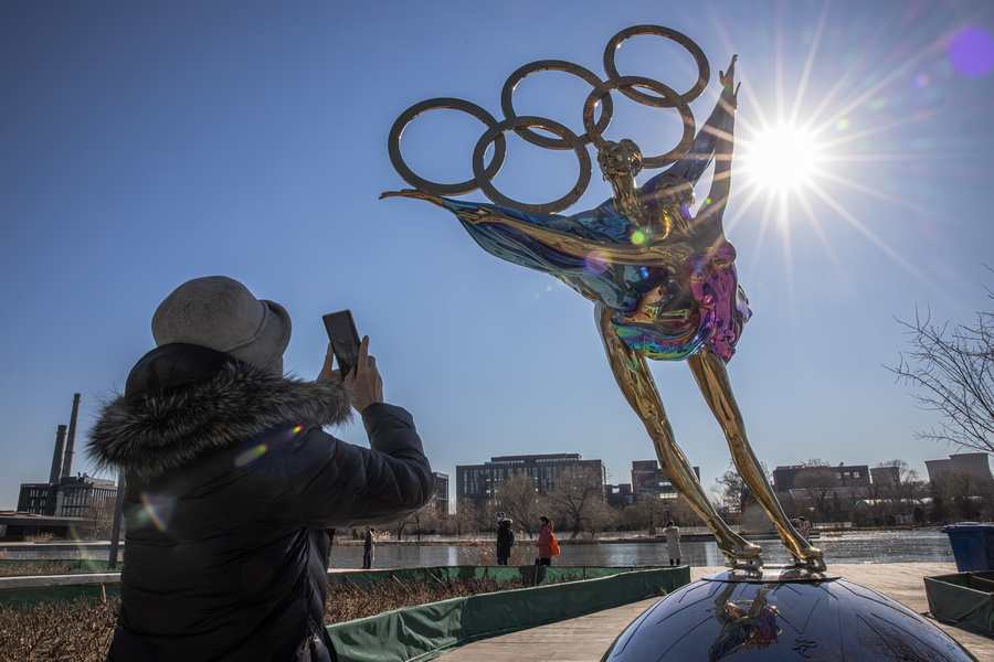 epaselect epa09614026 A woman takes photos with her mobile phone of a figure skating sculpture erected for the Beijing 2022 Winter Olympics, at the Shougang Industrial Park, which will be used as a venue for hosting sport and other events during Beijing 2022 Winter Olympics, in Beijing, China, 01 December 2021. According to China's epidemiologist experts, the new Omicron COVID-19 variant, which poses a high risk globally, at this moment wouldn't have a strong impact on China, which is scheduled in two months to host The 2022 Beijing Winter Olympics followed by the Paralympics.  EPA