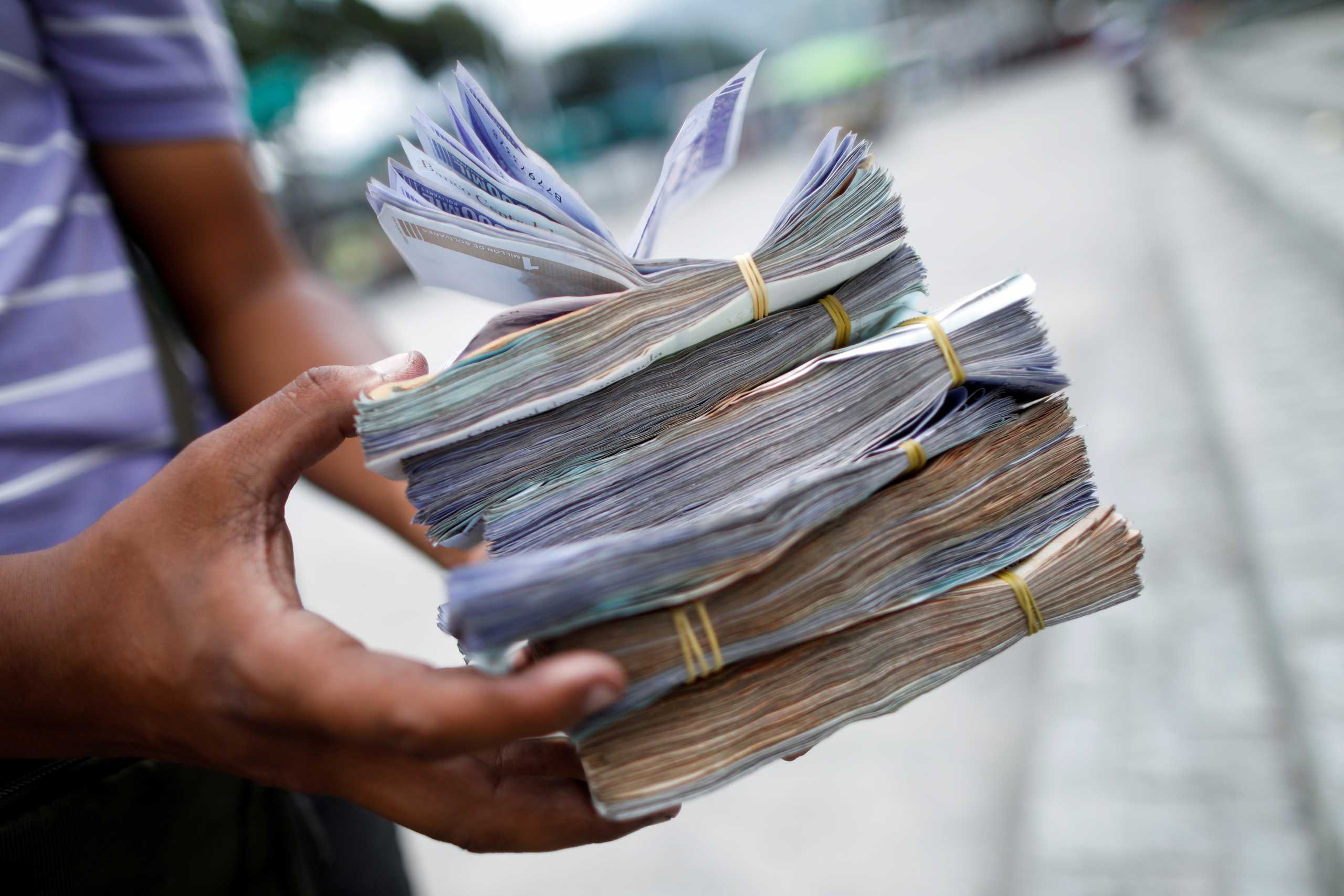 FILE PHOTO: The assistant of a bus driver holds Bolivar banknotes, worth between 0.01 and 0.25 US Dollars, after Venezuela's central bank announced it will cut six zeros from prices, in Caracas, Venezuela August 5, 2021. REUTERS