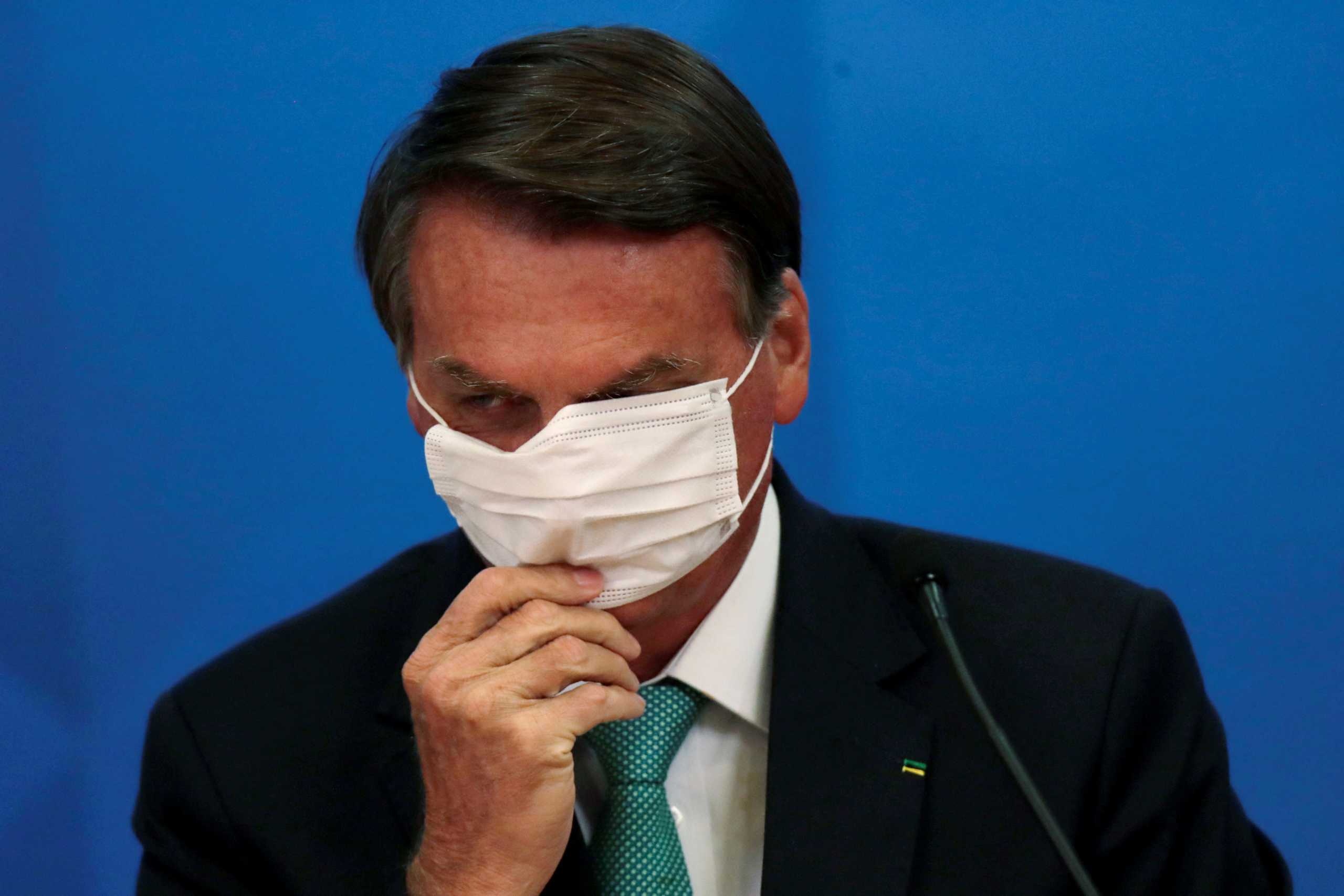 FILE PHOTO: Brazil's President Jair Bolsonaro adjusts his protective face mask during a ceremony of signing the Vaccine Technology Transfer Agreement for Oxford