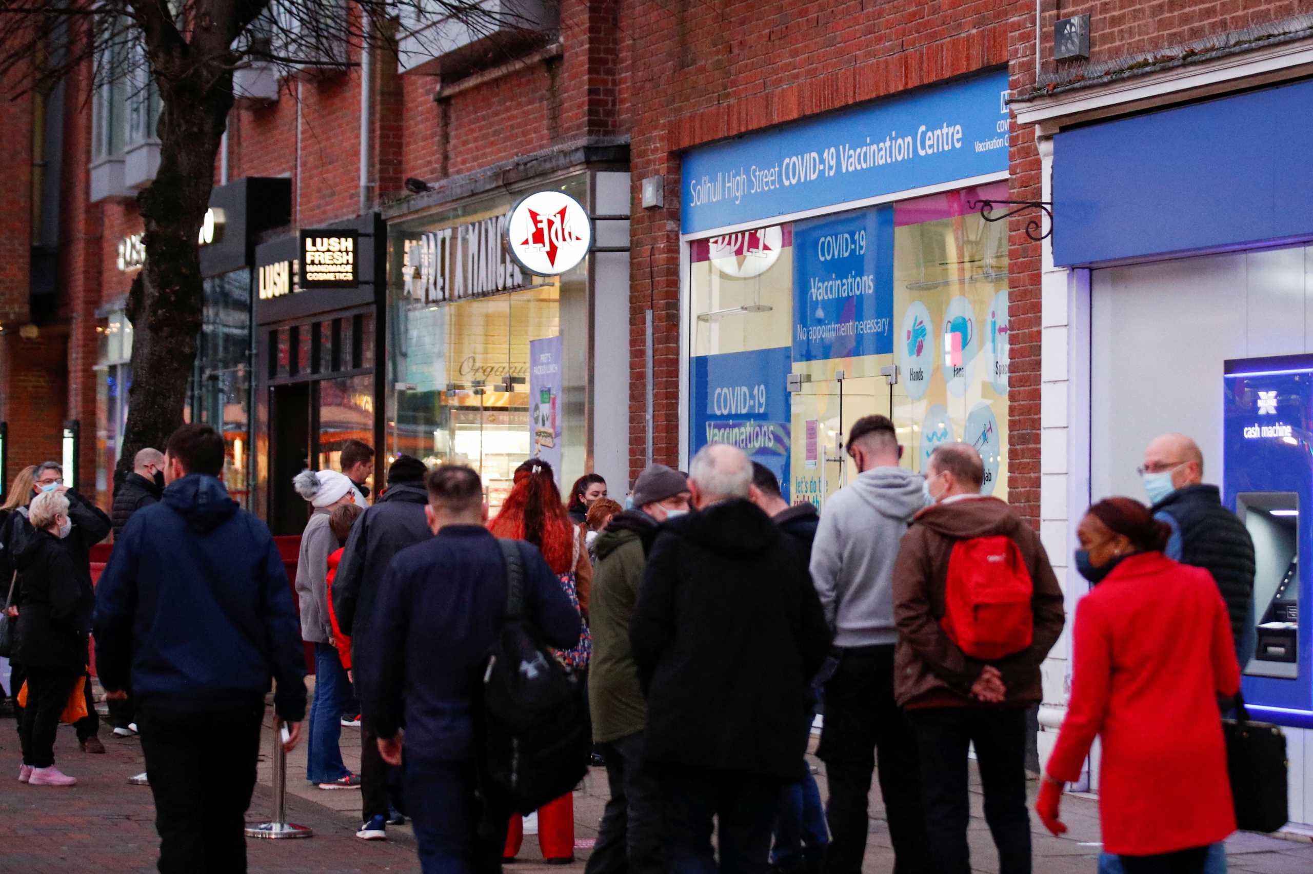People walk past a queue of people waiting to receive COVID-19 vaccine and booster doses, as the spread of the coronavirus disease (COVID-19) continues, at a walk-in vaccination centre, in Solihull, Britain, December 14, 2021. REUTERS
