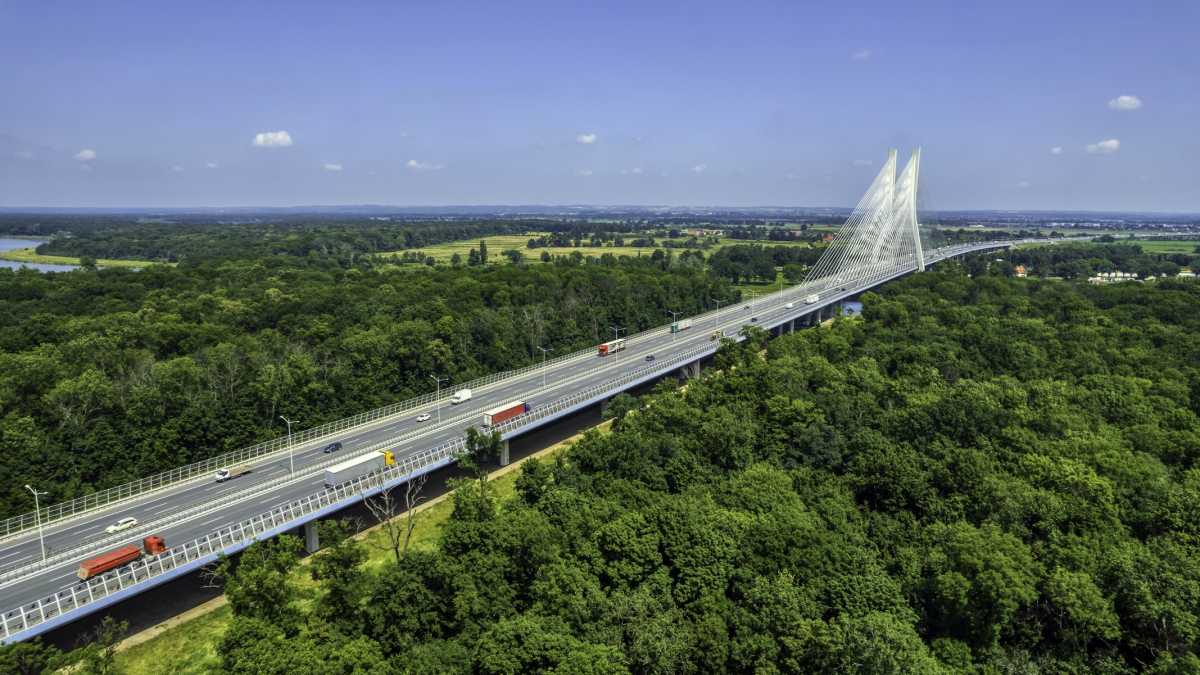 highway crossing the green forest with the cable-stayed bridge on a horizon