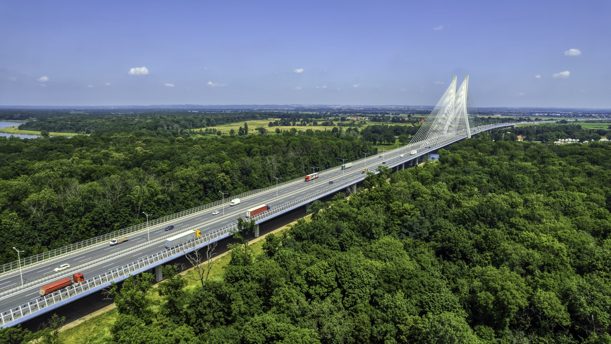 highway crossing the green forest with the cable-stayed bridge on a horizon