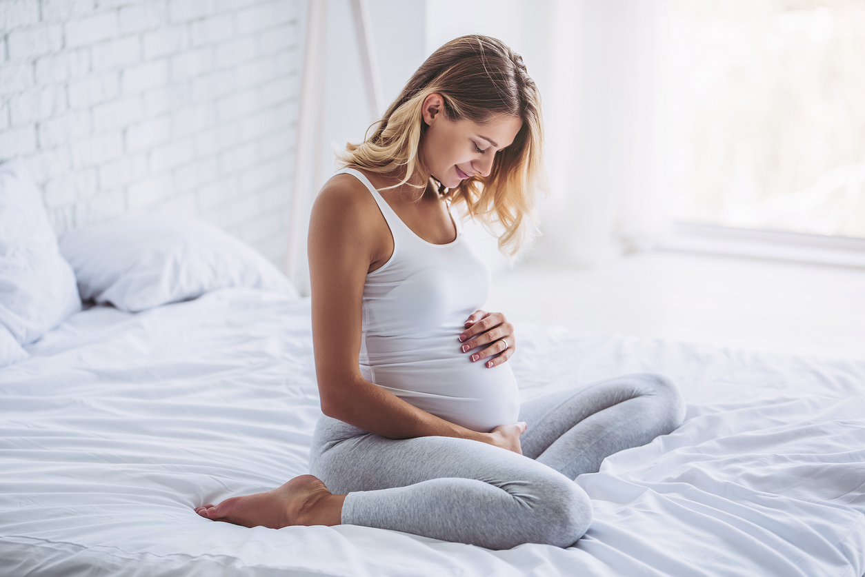 Attractive pregnant woman is sitting in bed and holding her belly. Last months of pregnancy.