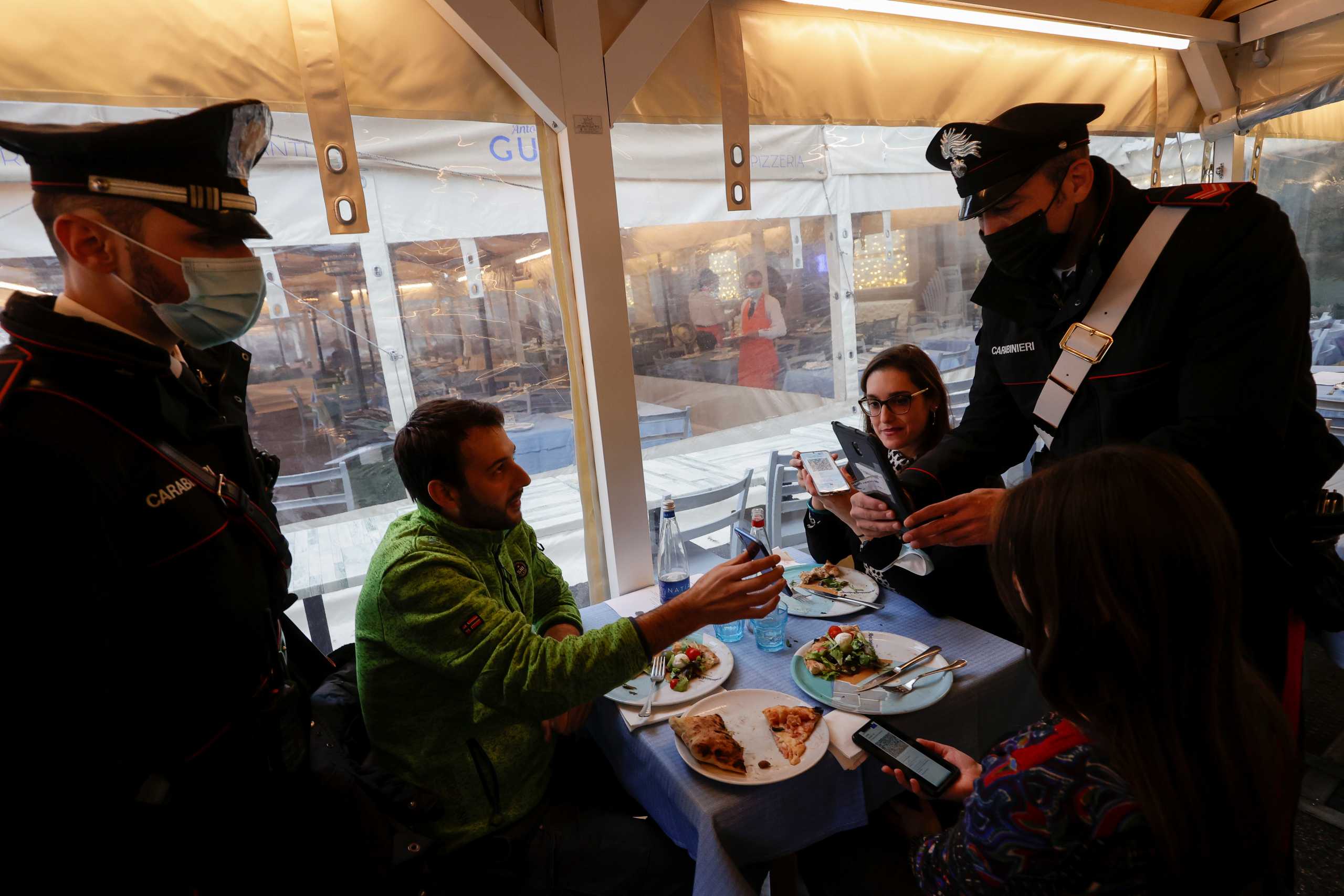 Carabinieri officer checks the coronavirus disease (COVID-19) health passes, known as a Green Pass, of a group of people in a restaurant the day the government restricts access of unvaccinated, in Naples, Italy December 6, 2021. REUTERS