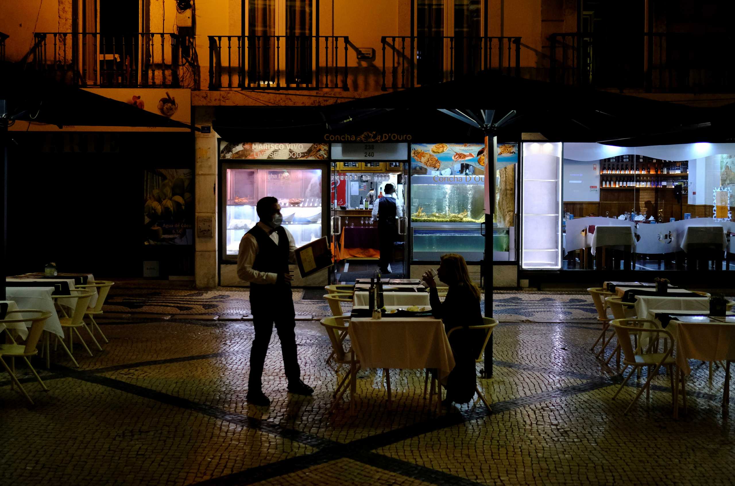 FILE PHOTO: A waiter wearing a face mask talks with a woman as she eats on an empty terrace of a restaurant at Augusta street, amid the coronavirus disease (COVID-19) pandemic, in Lisbon, Portugal, July 28, 2021. REUTERS