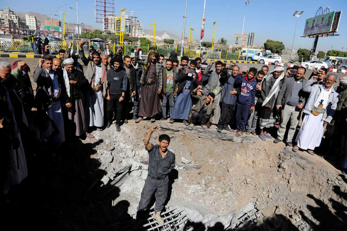 People react as they gather around a crater caused by a Saudi-led airstrike on a road in Sanaa, Yemen, December 23, 2021. REUTERS