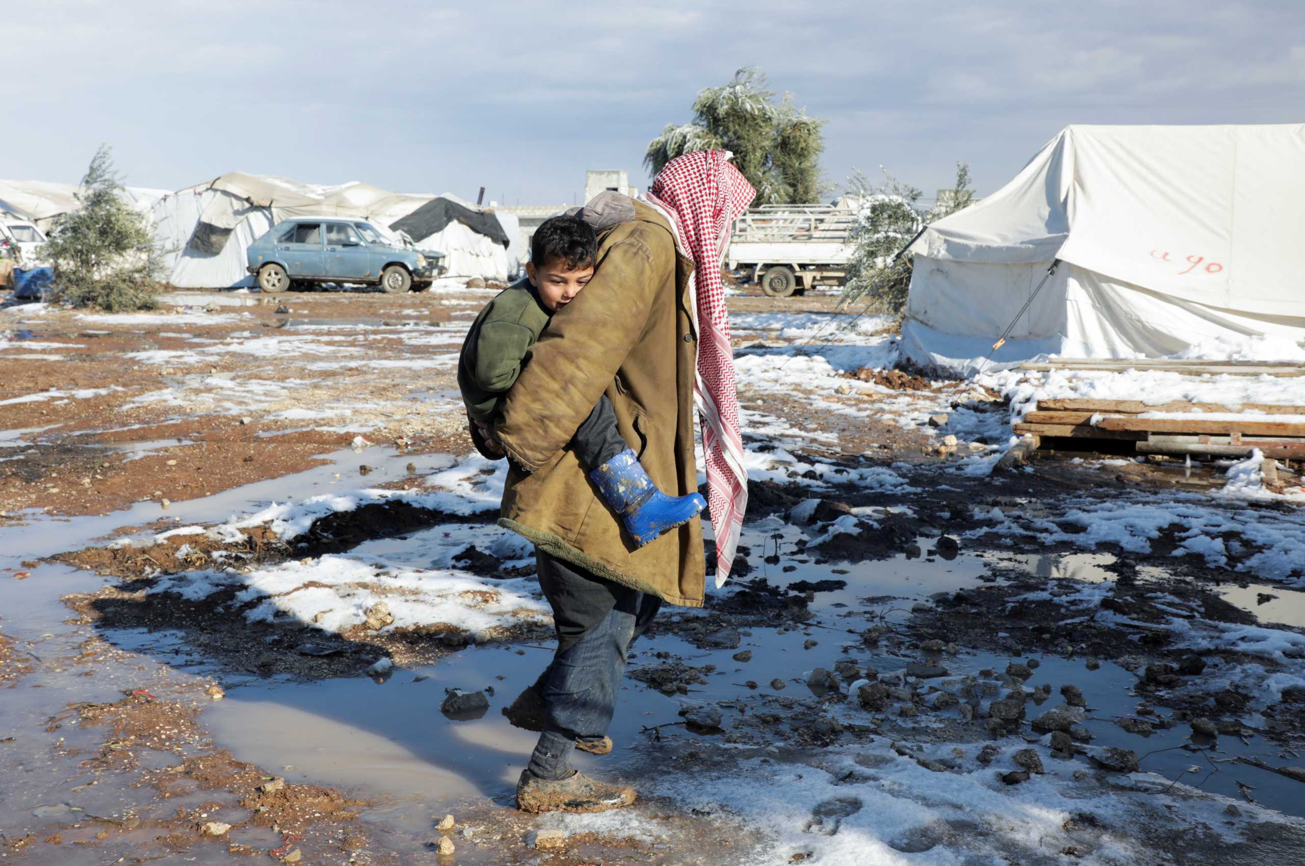 A internally displaced man carries a child as he walks through mud and snow at a camp in northern Aleppo countryside, Syria January 19, 2022. Picture taken January 19, 2022. REUTERS