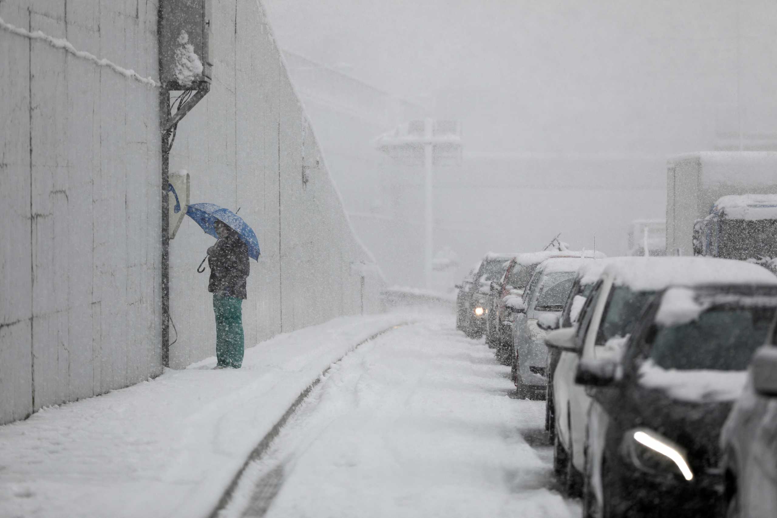 A person holding an umbrella stands next to vehicles stuck in traffic in the Attiki Odos motorway, during heavy snowfall in Athens, Greece, January 24, 2022. REUTERS