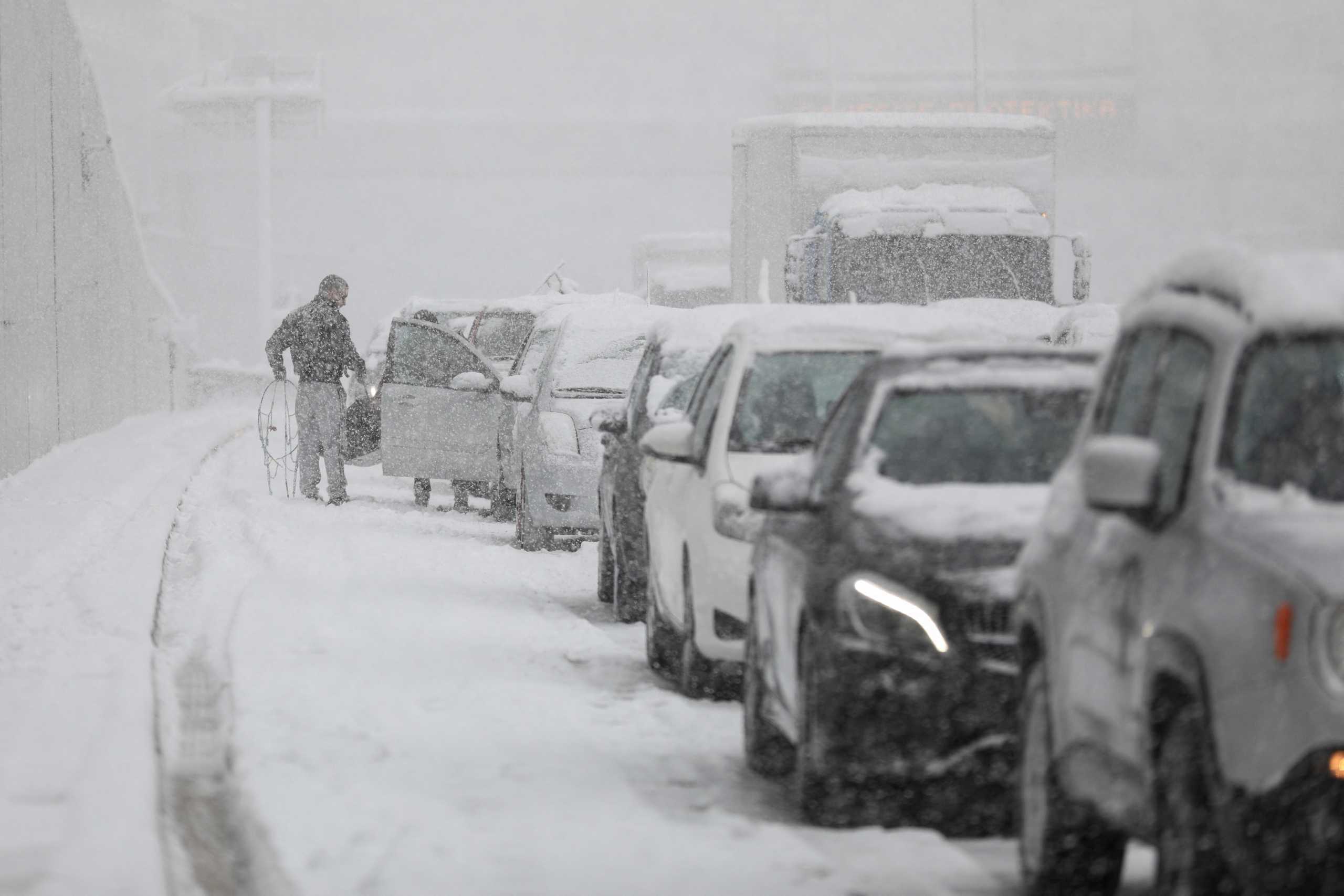 A man prepares to put snow chains in his car, as vehicles are stuck in traffic in the Attiki Odos motorway, during heavy snowfall in Athens, Greece, January 24, 2022. REUTERS