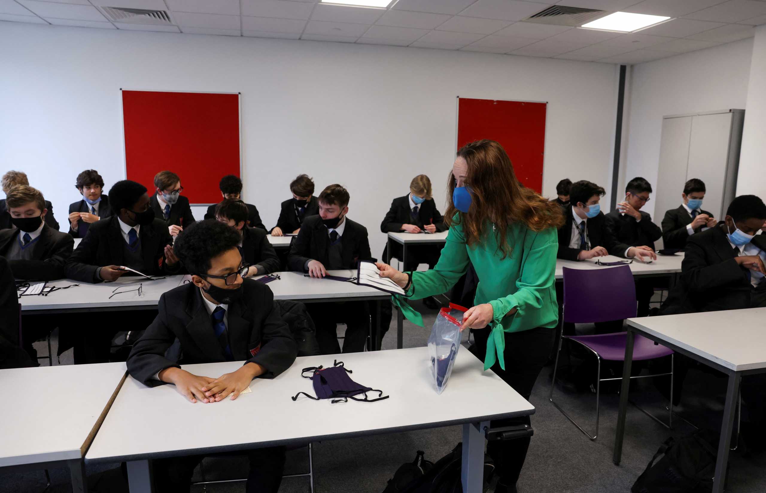 FILE PHOTO: A teacher hands out face masks to students on the first day back at school, as the coronavirus disease (COVID-19) lockdown begins to ease, at Fulham Boys School in London, Britain, March 8, 2021. REUTERS