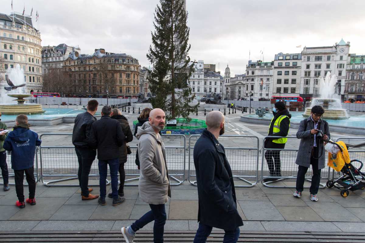 People walk and stand by the temporary fencing around the perimeter of Trafalgar Square, to prevent crowds gathering on New Year's Eve, in London, Britain, December 31, 2021. REUTERS