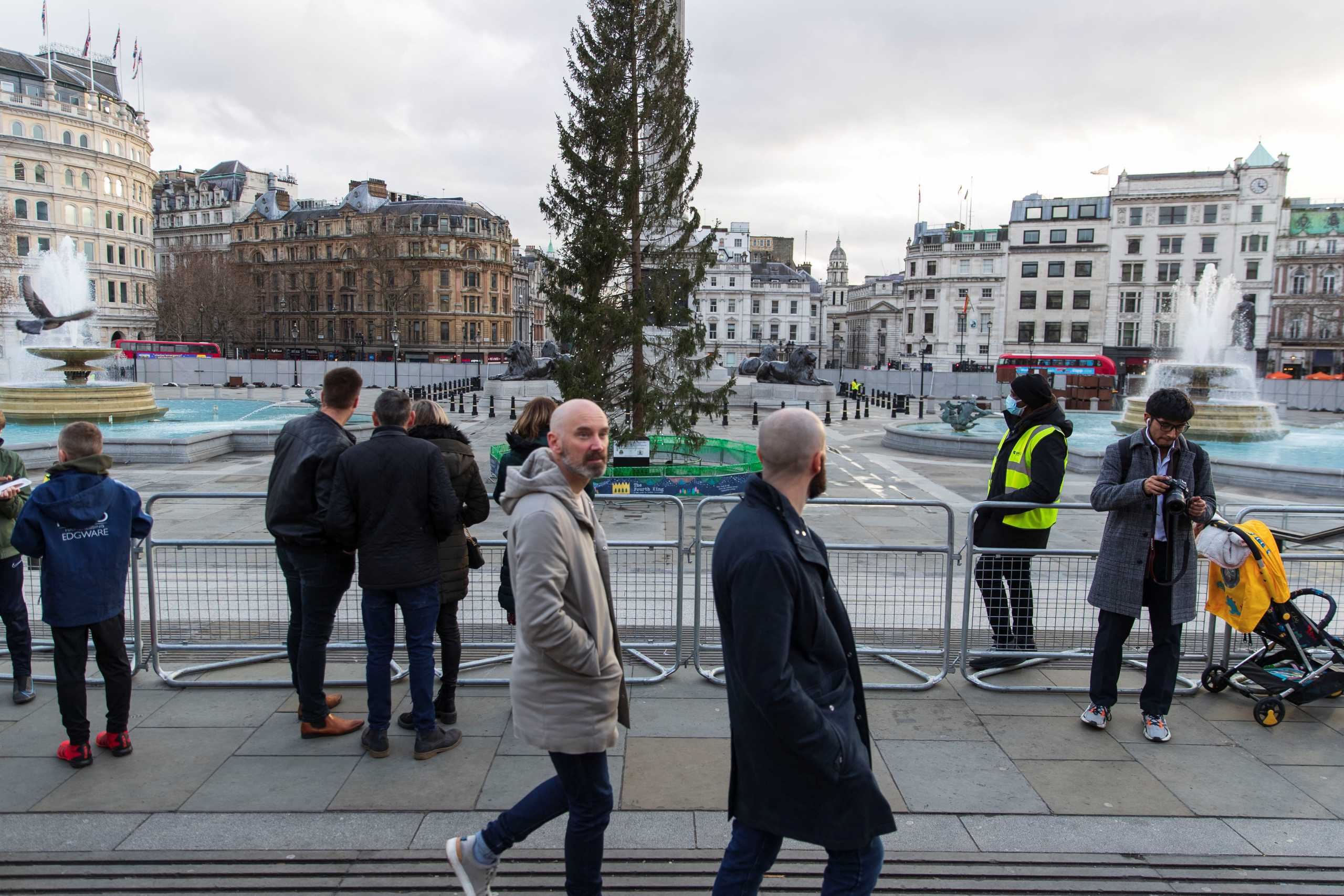 People walk and stand by the temporary fencing around the perimeter of Trafalgar Square, to prevent crowds gathering on New Year's Eve, in London, Britain, December 31, 2021. REUTERS