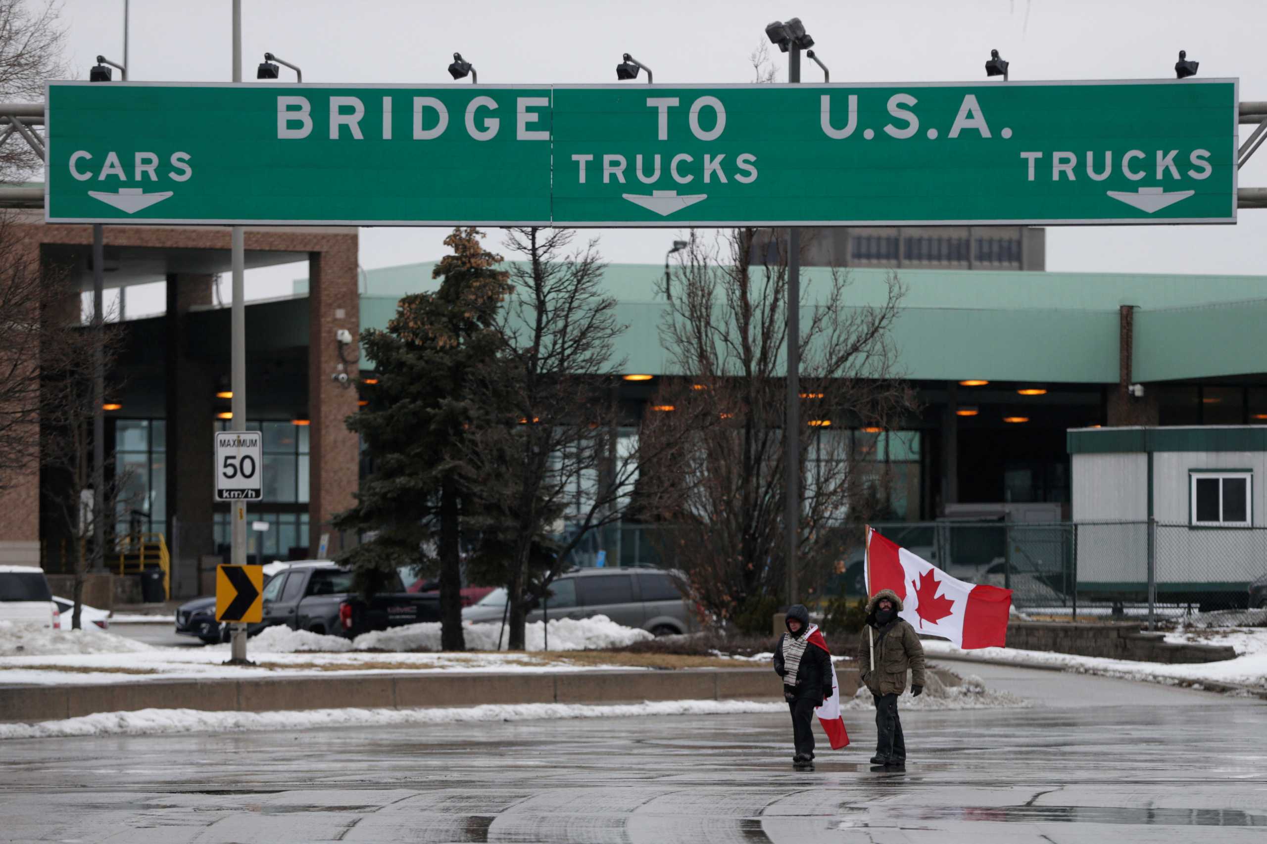 People walk with Canadian flags as truckers and supporters continue blocking access to the Ambassador Bridge, which connects Detroit and Windsor, in protest against coronavirus disease (COVID-19) vaccine mandates, in Windsor, Ontario, Canada February 11, 2022. REUTERS