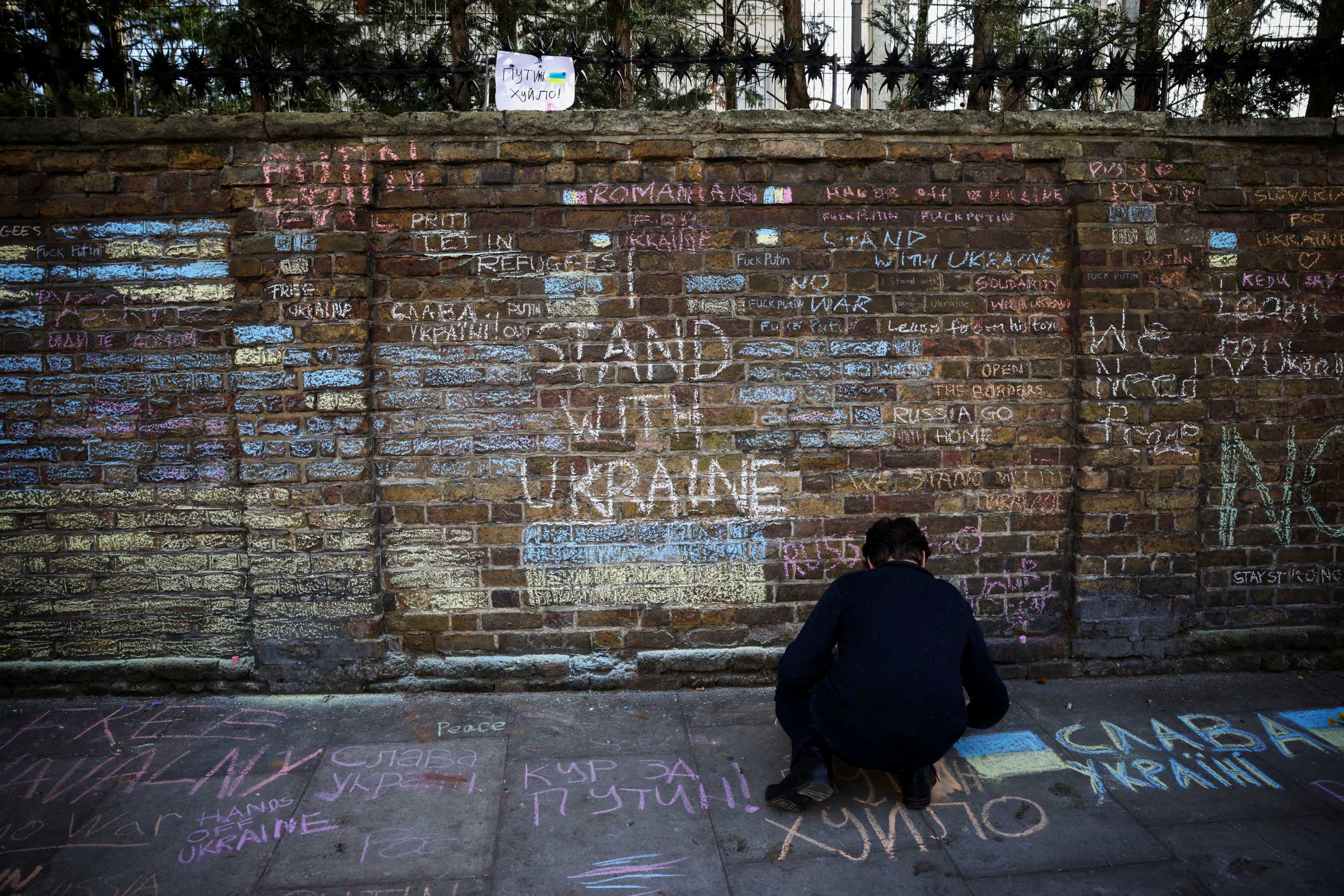 A protester writes on a pavement in front of signs on the wall of the Russian Embassy during an anti-war protest, after Russia launched a massive military operation against Ukraine, in London, Britain, February 26, 2022. REUTERS