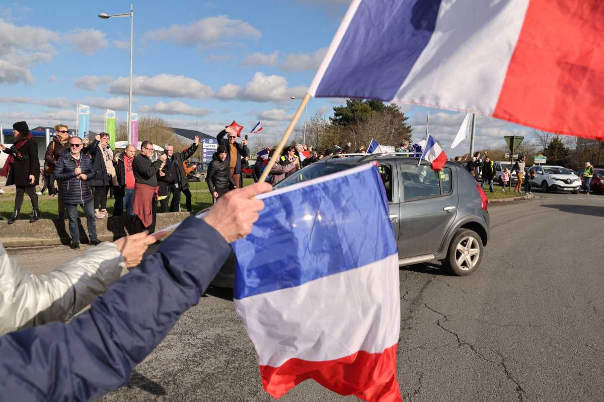 Supporters and members of the yellow vest movement hold French national flag on a parking lot of a shopping center in Longueau as they cheer French anti-COVID restrictions car drivers during their "Convoi de la liberte" (The Freedom Convoy), a vehicular convoy protest converging on Paris to protest coronavirus disease (COVID-19) vaccine and restrictions in France, February 11, 2022. REUTERS