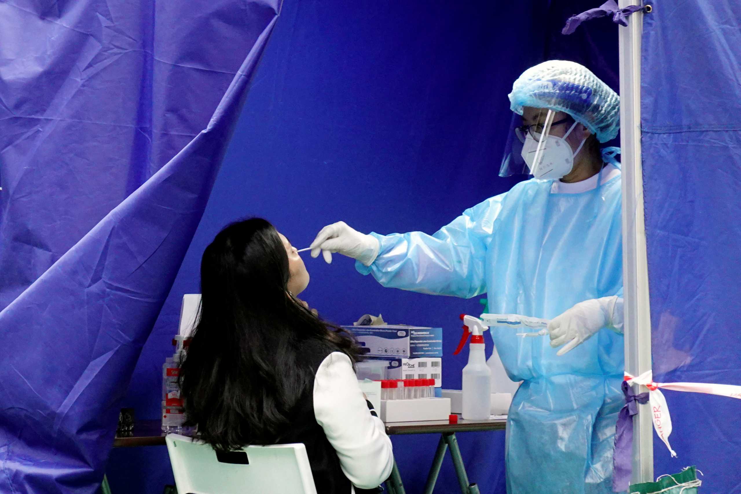 A medical worker collects a nasal swab sample from a woman at a makeshift testing site for the coronavirus disease (COVID-19), following the outbreak in Hong Kong, China February 18, 2022. REUTERS