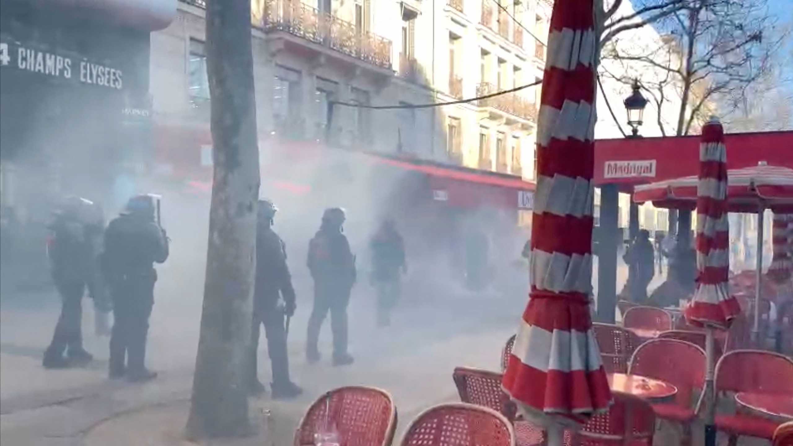 Riot police stand amidst tear gas next to a terrace on the Champs-Elysees avenue, as they try to disperse demonstrators during a protest against coronavirus disease (COVID-19) vaccine and restrictions, in Paris, France, February 12, 2022, in this screen grab taken from a video. Video taken February 12, 2022. Clement Lanot