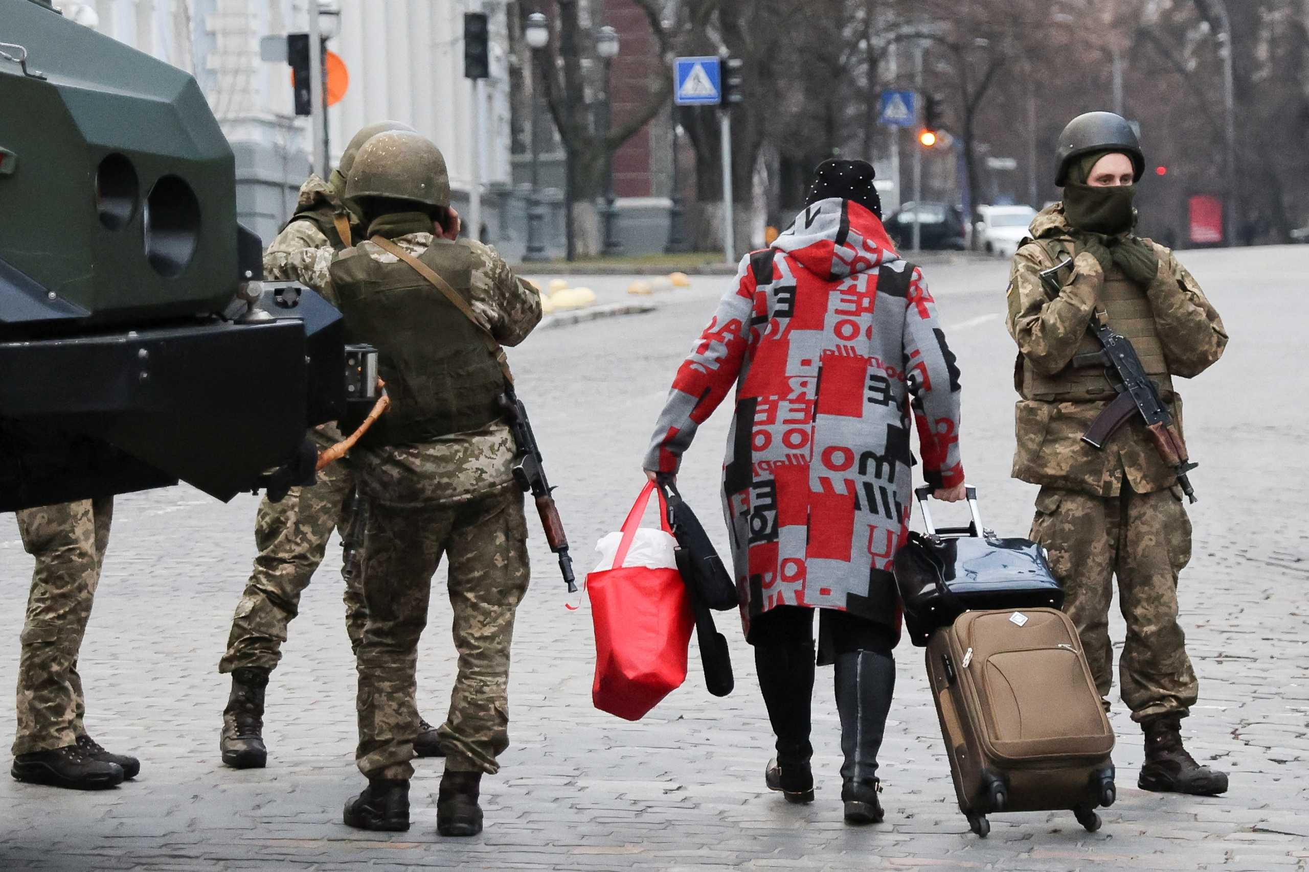 A woman walks past Ukrainian military service members guarding a road that leads to a government block, after Russian President Vladimir Putin authorized a military operation in eastern Ukraine, in Kyiv, Ukraine, February 24, 2022. REUTERS