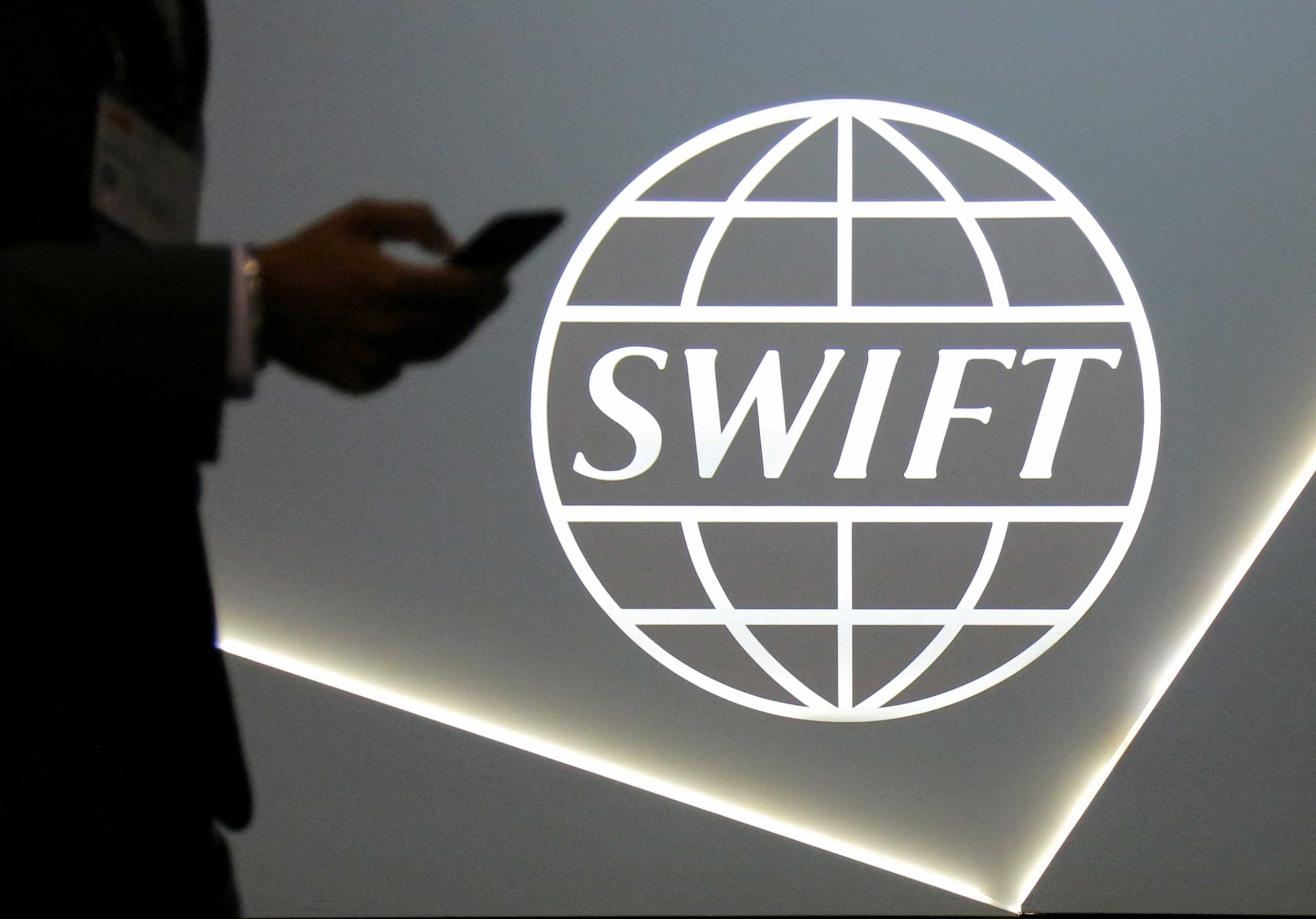 FILE PHOTO: A man using a mobile phone passes the logo of global secure financial messaging services cooperative SWIFT at the SIBOS banking and financial conference in Toronto, Ontario, Canada October 19, 2017.  REUTERS