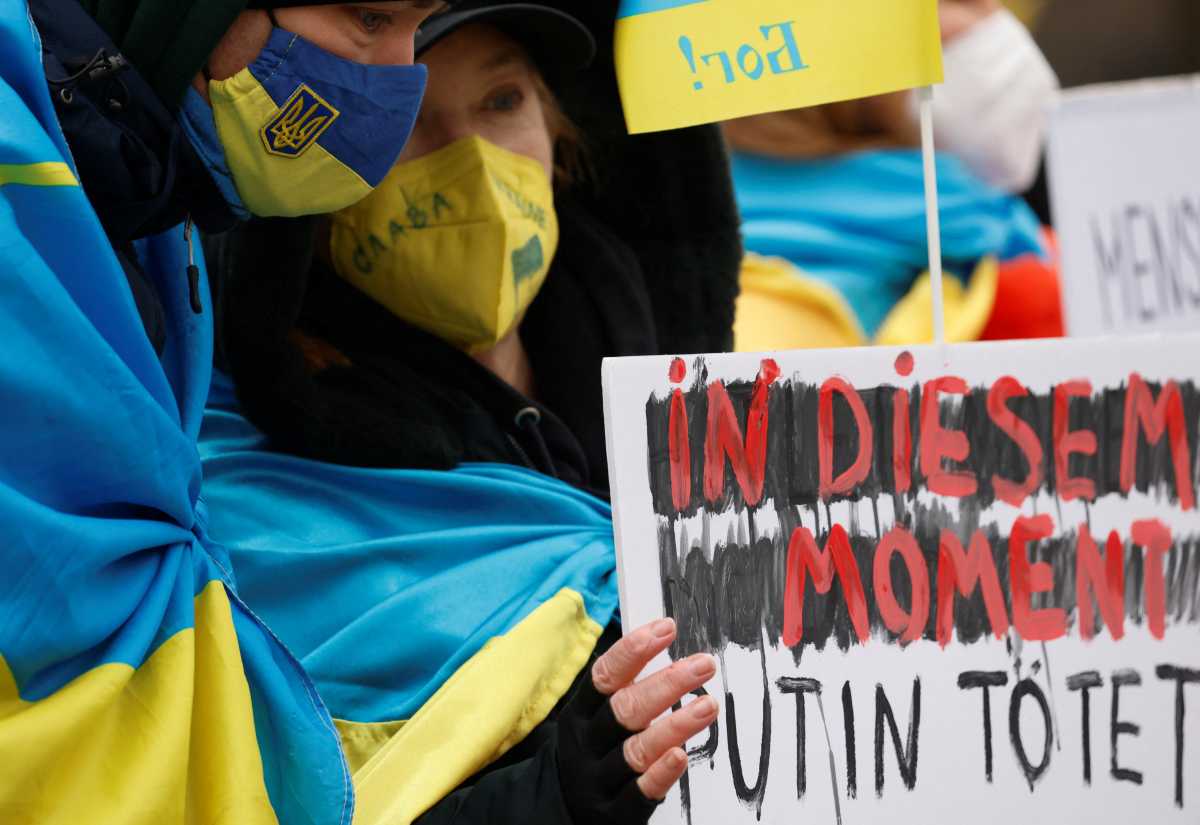 Demonstrators, of which one is holding a placard reading "at that moment, Putin kills", wearing Ukrainian flags, protest outside the German chancellery, after Russia launched a massive military operation against Ukraine, in Berlin, Germany, February 25, 2022. REUTERS