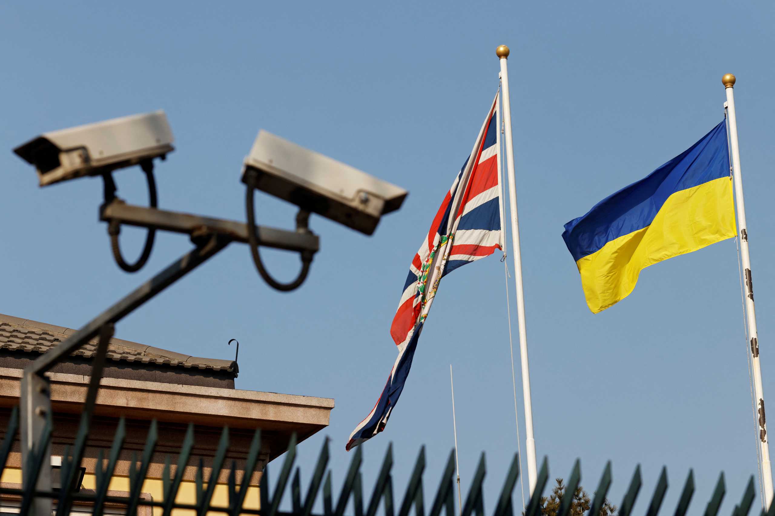 Surveillance cameras are seen near the flags of Ukraine and Union Jack fluttering at the British embassy in Beijing, China February 25, 2022. REUTERS